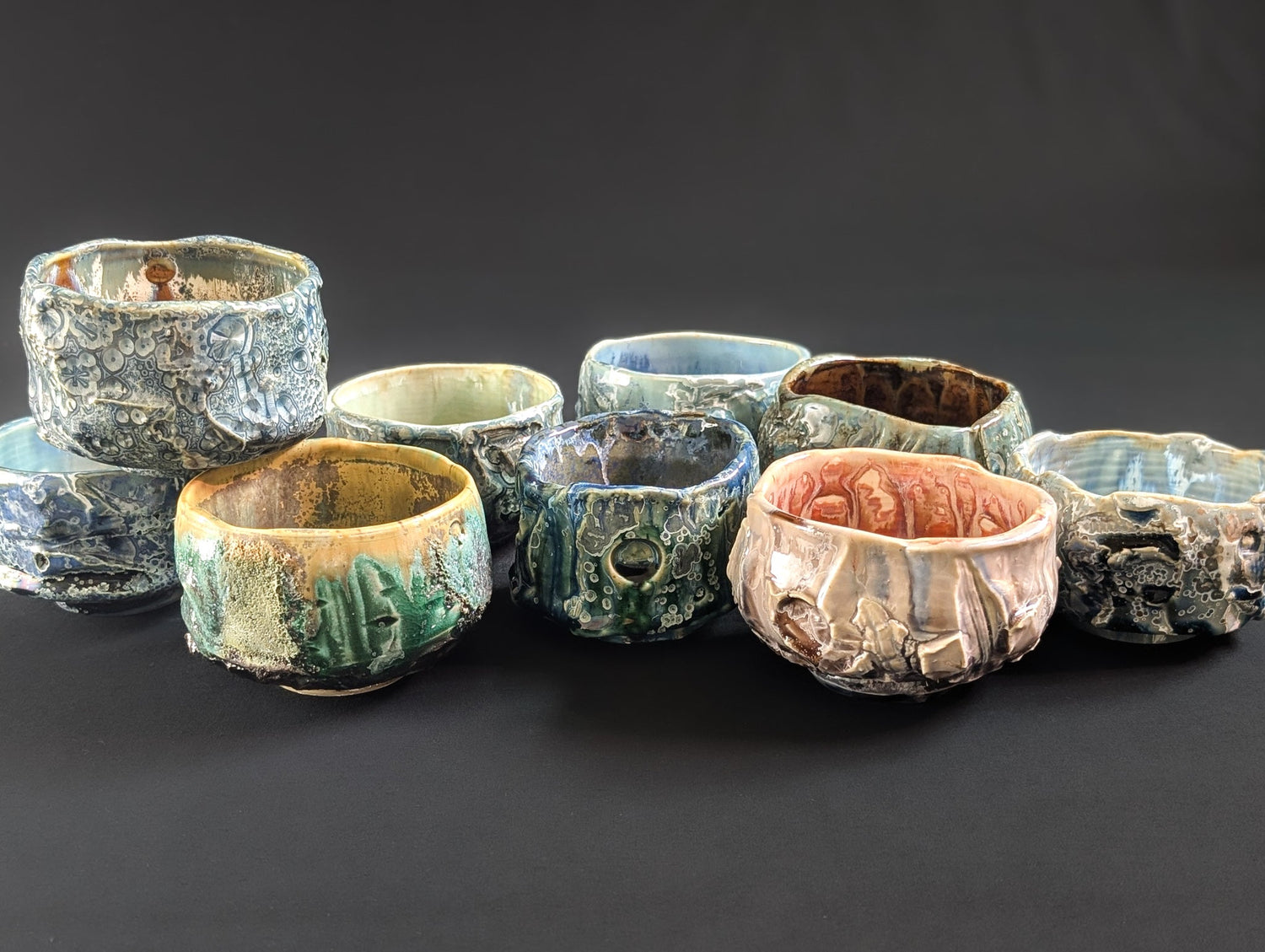 A vibrant collection of Robbin Harris’s chawan tea bowls, showcasing a rich variety of colors and crystalline glazes, arranged side by side in a front-facing view.