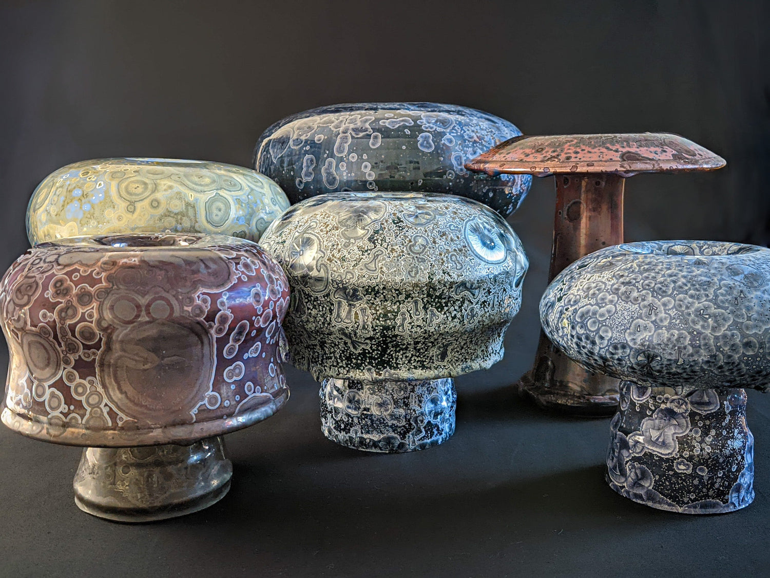Group shot of the Mushroom Collection by Robbin Harris Ceramics, showcasing various sculptural mushroom-inspired vases with intricate crystalline glazes against a black background.