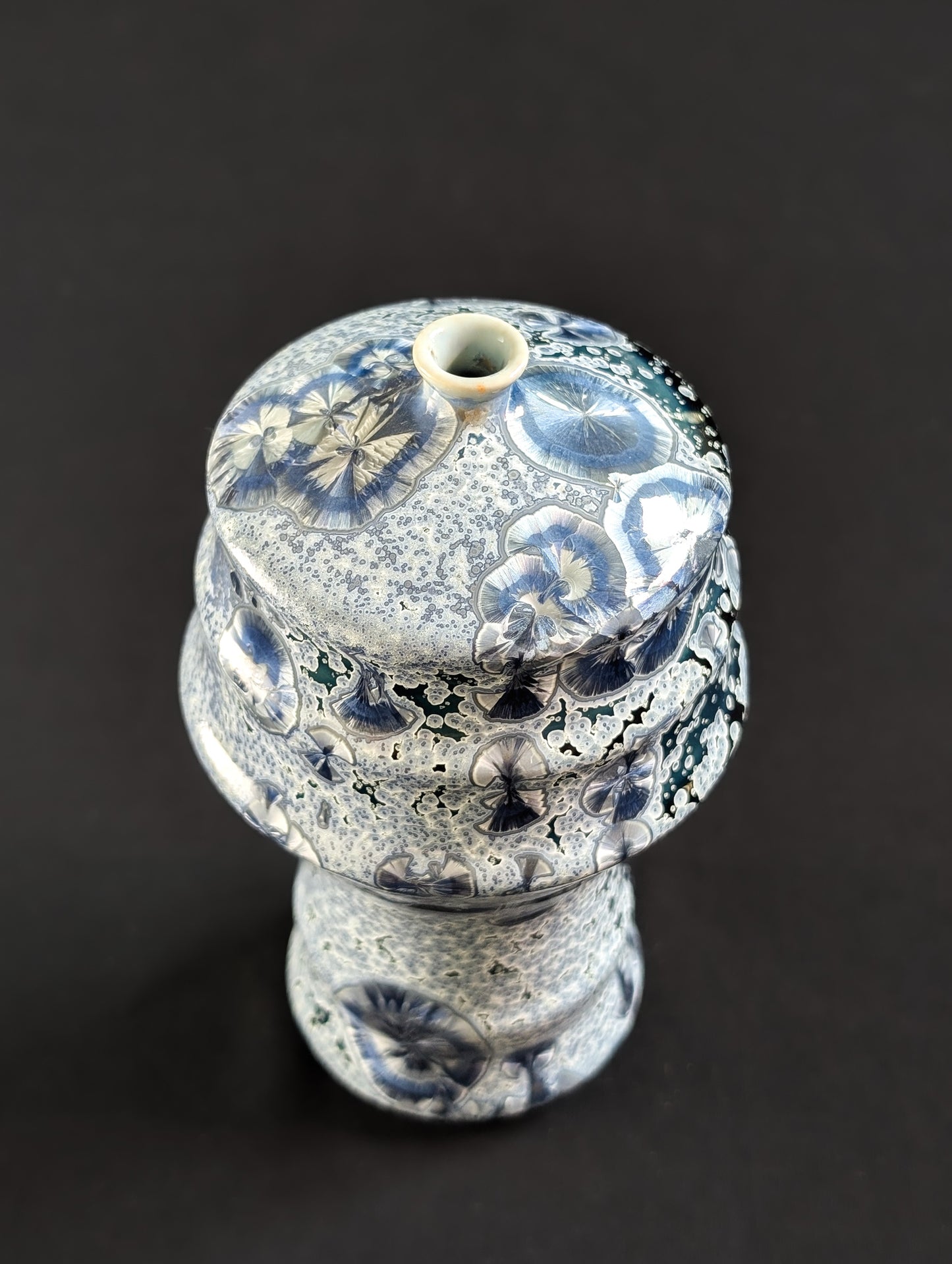 "Tall, narrow-neck crystalline vase with flowing curves and a deep midnight blue glaze, covered in intricate silver and lavender crystal formations, shown against a dark background.