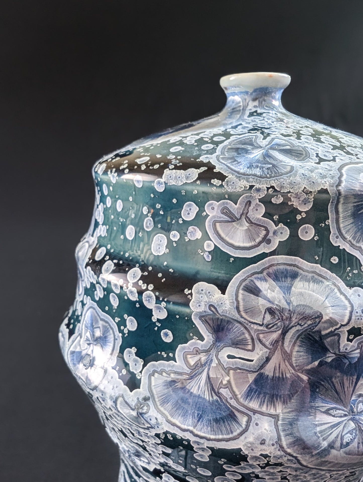 Close-up of the upper section of a crystalline vase, showing detailed silver and lavender crystal blooms floating on a rich midnight blue glaze.