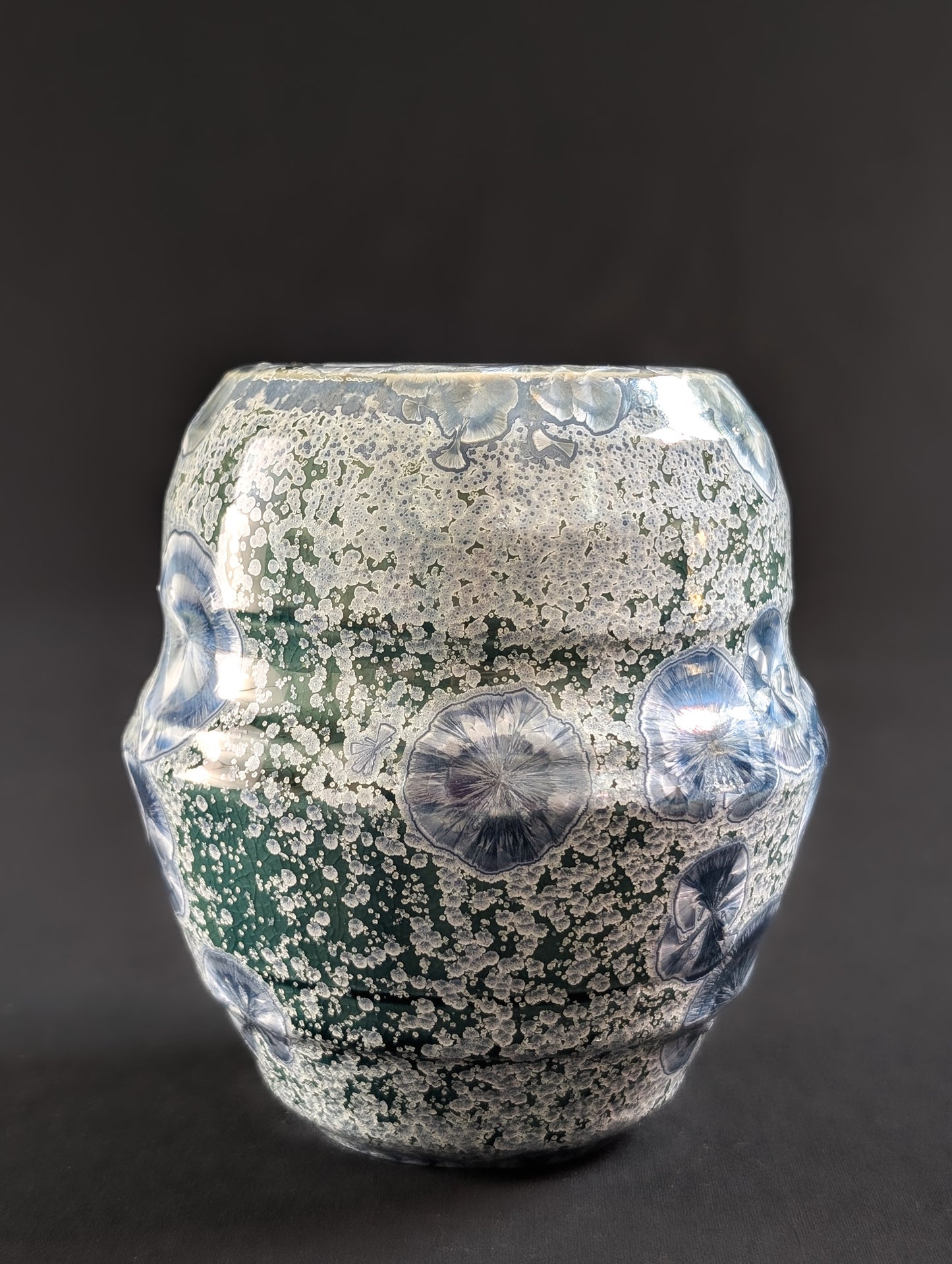 Decorative crystalline vase with a surface of large sapphire crystals, small silver secondary crystals on an emerald green background.