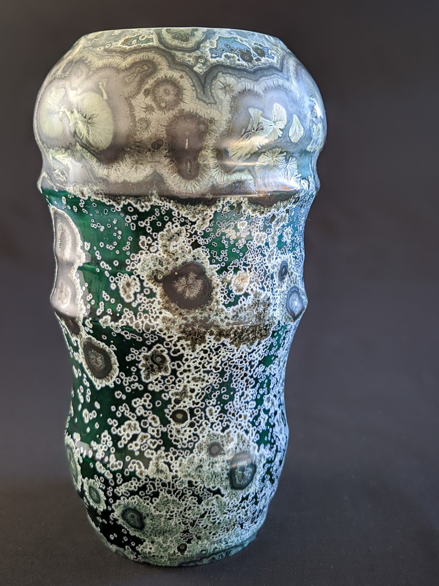 Front view of emerald green ceramic vase showcasing flowing curves, geometric facets, and a rich over crystallized surface texture.
