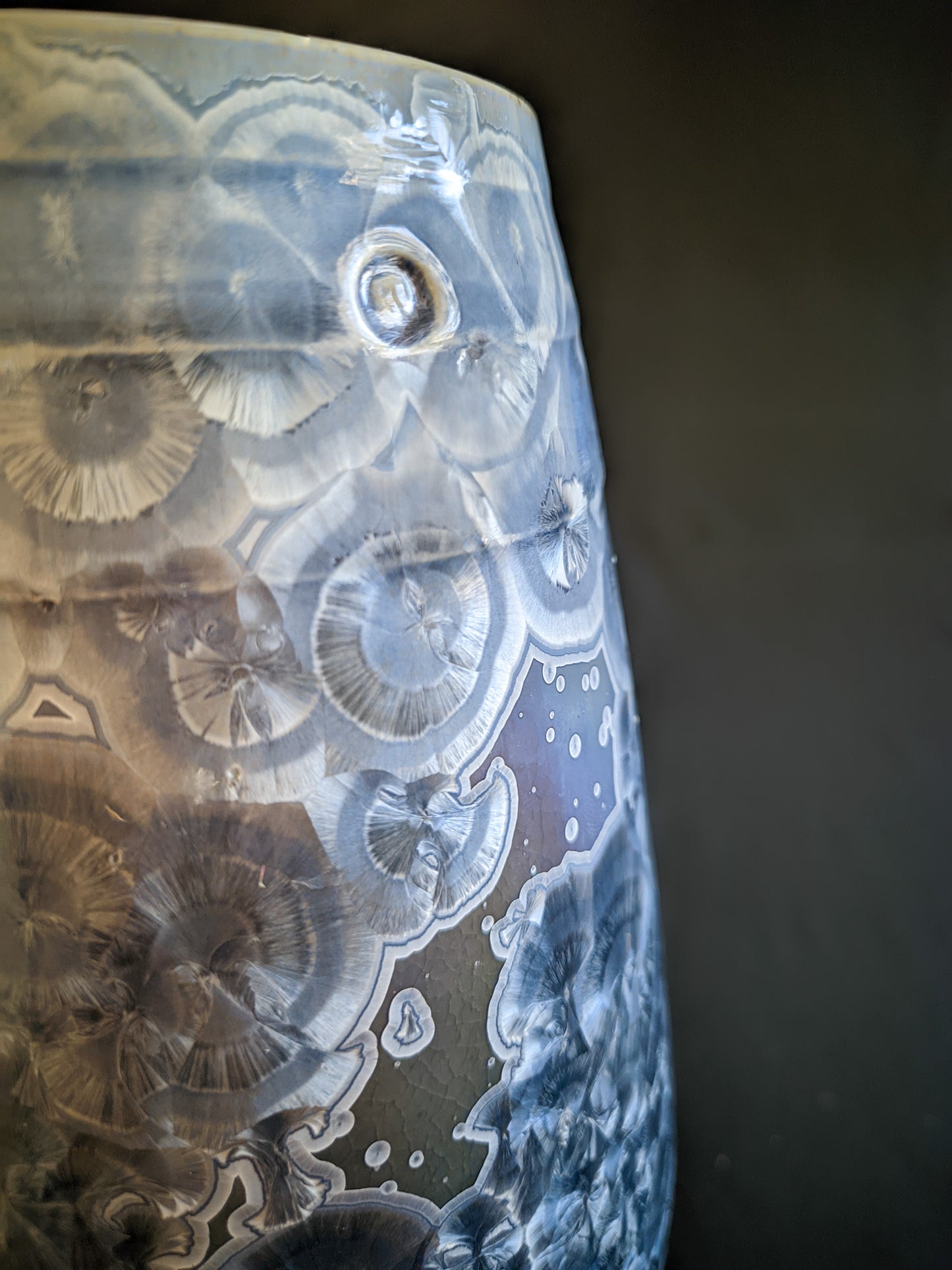 Close up of large, sculptural vase with a wide opening, showcasing a dramatic color gradient from dark blue to light purple and white. The vase is adorned with overcrystallized blue crystals with white rings, creating an artistic texture.