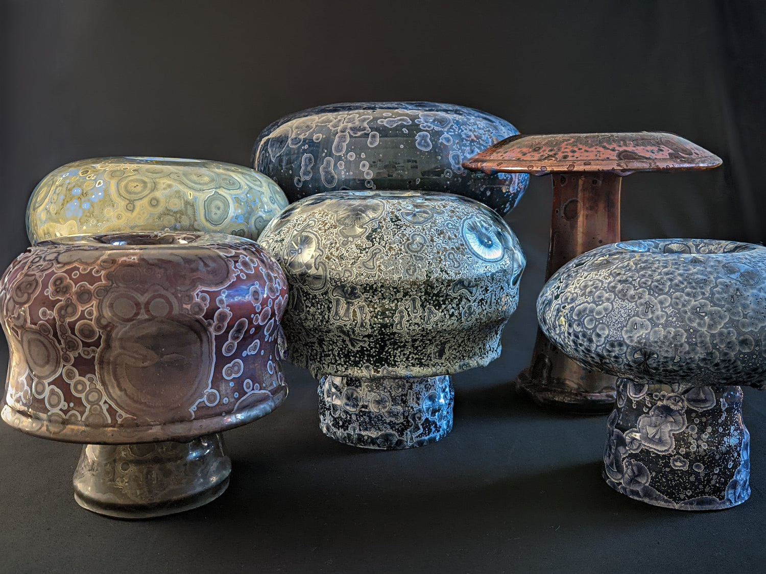 A collection of unique ceramic mushroom vases in various shapes and colors, set against a black backdrop, showcasing the artistry and craftsmanship of each piece.