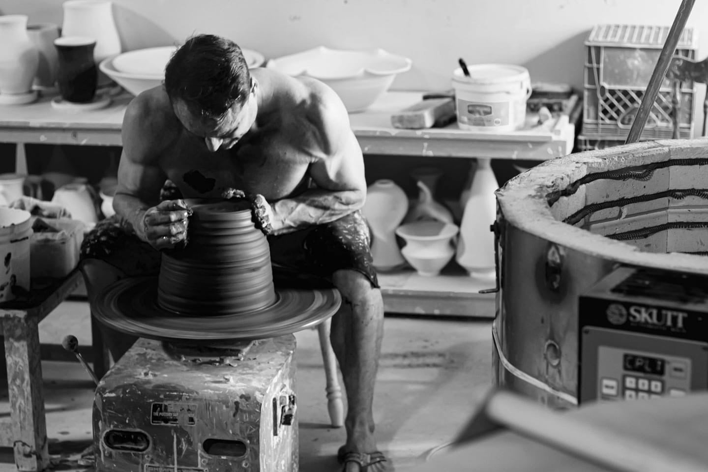 Robbin Harris shaping a large ceramic form on the potter's wheel, his hands expertly guiding the clay as it takes shape. Black and white photo by photographer David Marion.