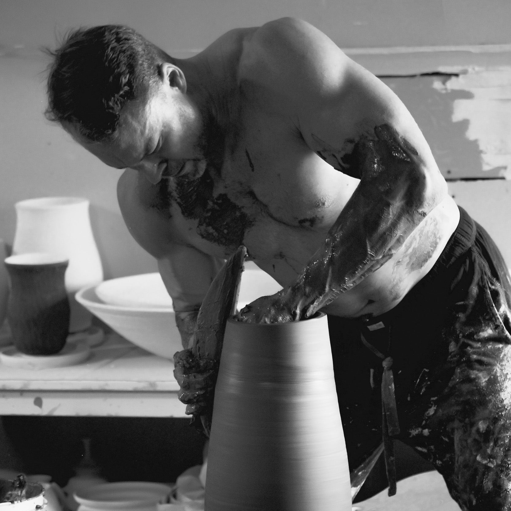 Side view of Robbin Harris throwing a large vessel on the wheel, his focused expression highlighting the precision and skill in his craft. Black and white photography by David Marion.