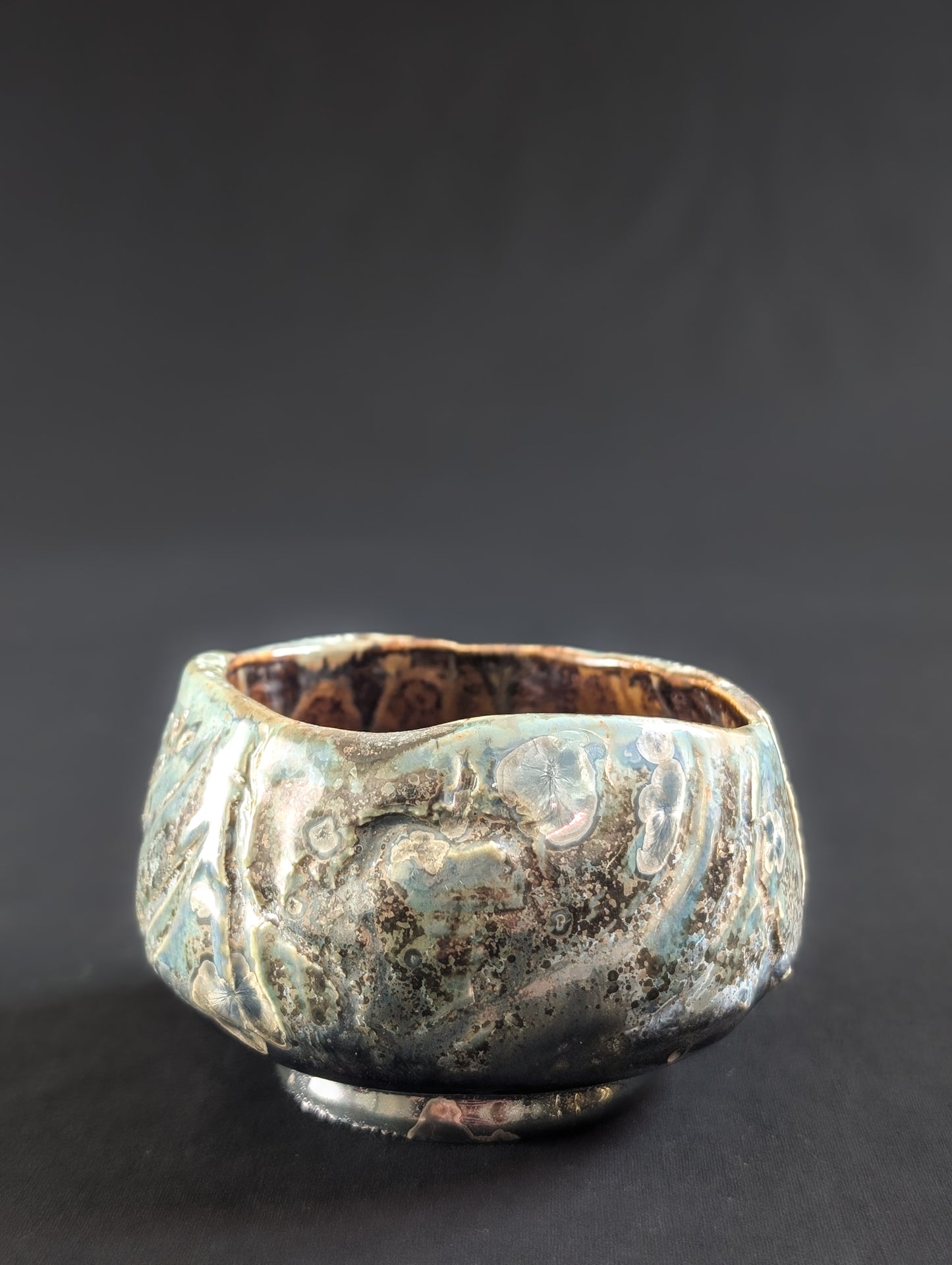 Side view of the tea bowl with flowing texture lines and scattered speckles of silver and brown.
