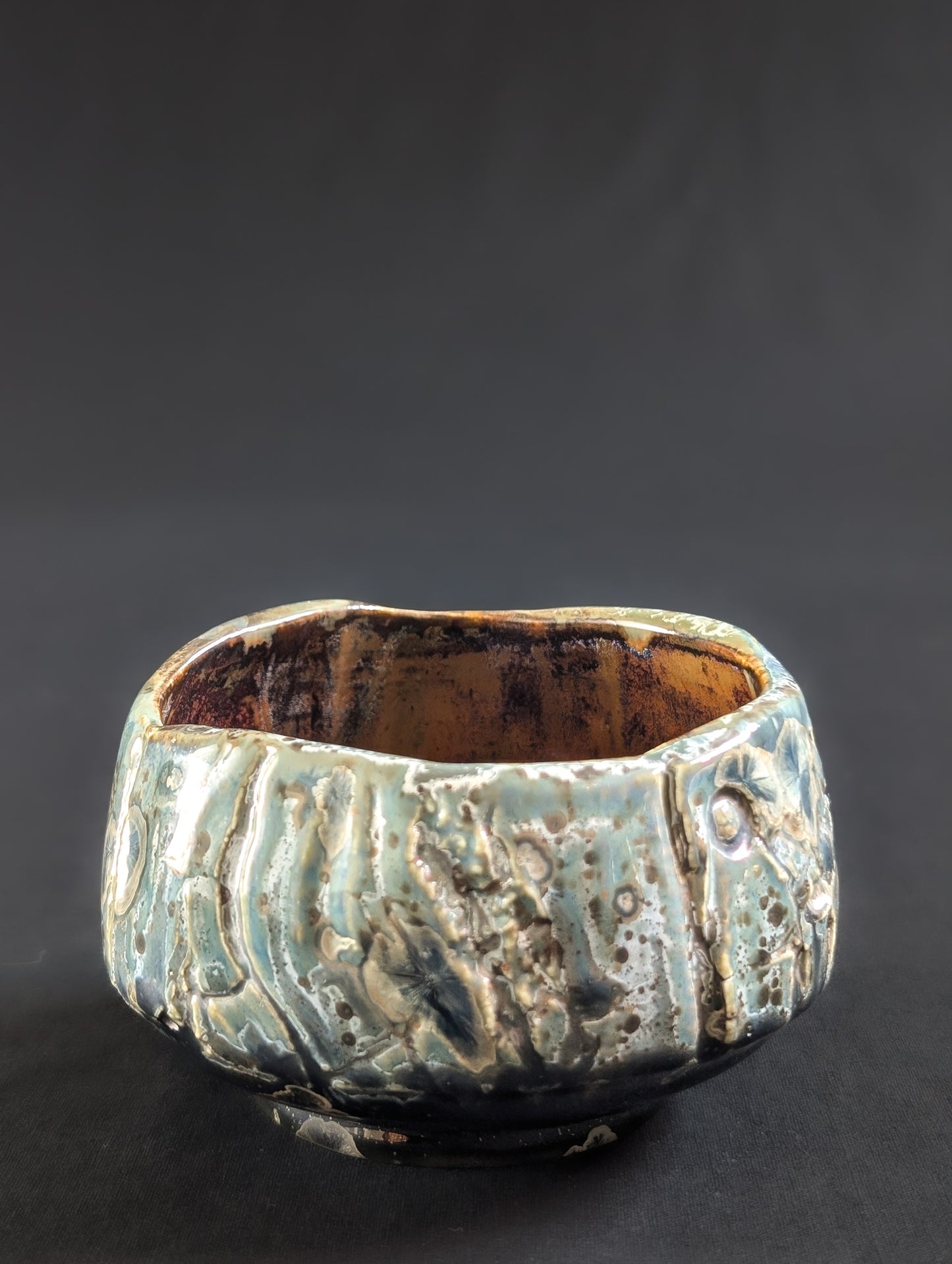 Side view of the tea bowl with flowing texture lines and scattered speckles of silver and brown.
