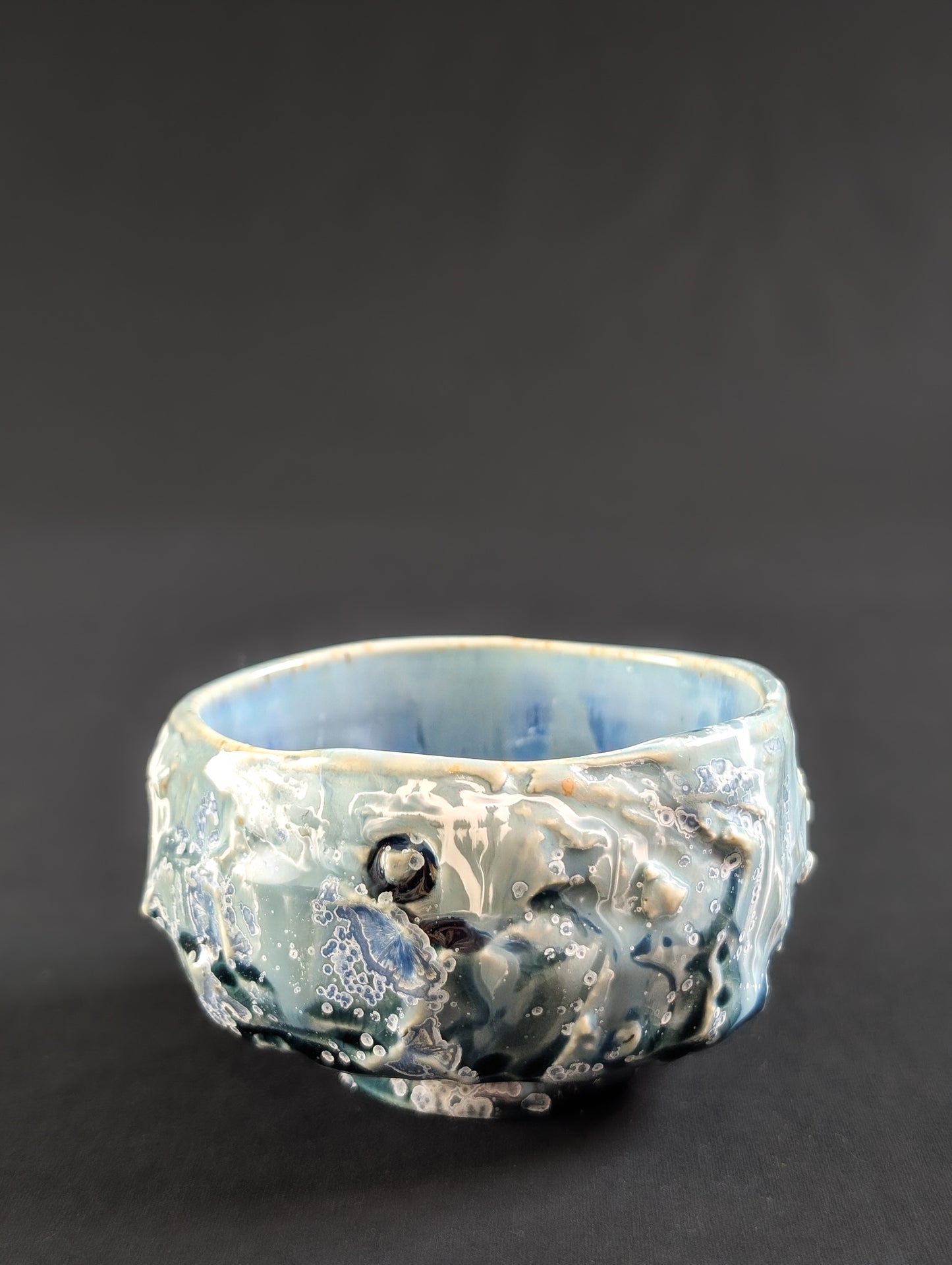 Side view of 'Caldera' chawan by Robbin Harris, showing textured, rock-like exterior in seafoam green and light blue glaze.