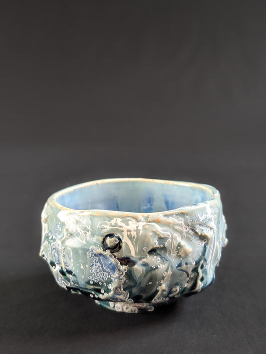 Side view of 'Caldera' chawan by Robbin Harris, showing textured, rock-like exterior in seafoam green and light blue glaze.