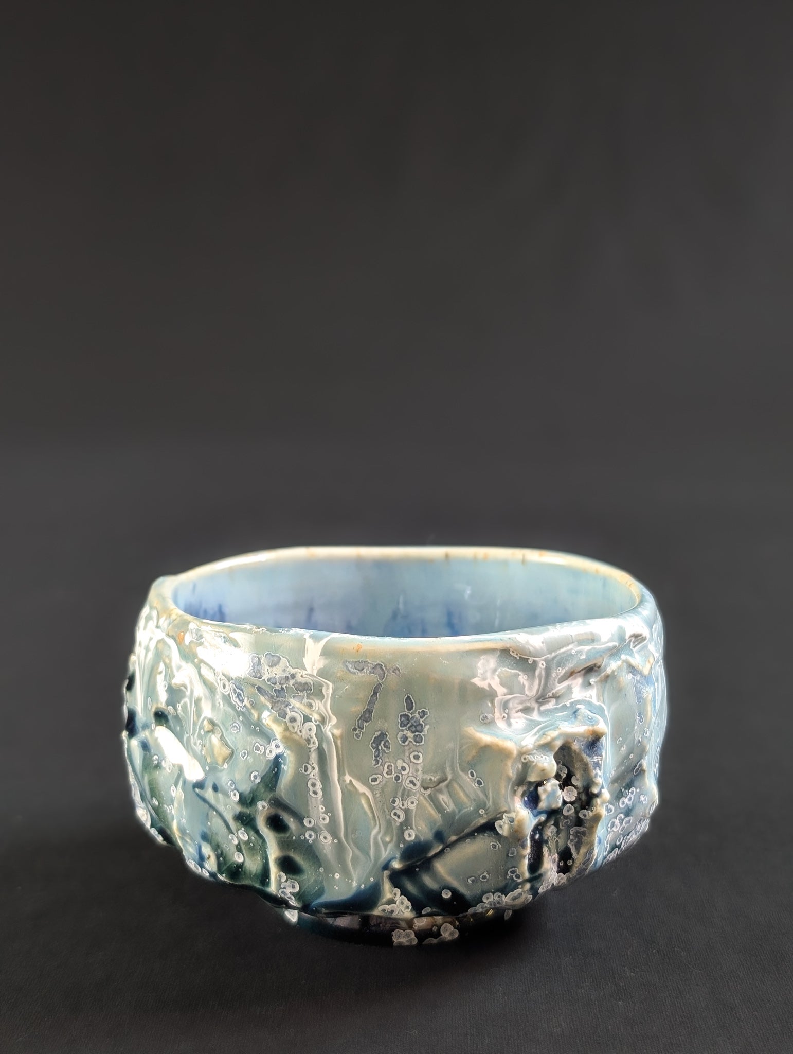 Angled profile of the chawan with glaze dripping over heavy carving, accented by tiny white-rimmed blue crystals.