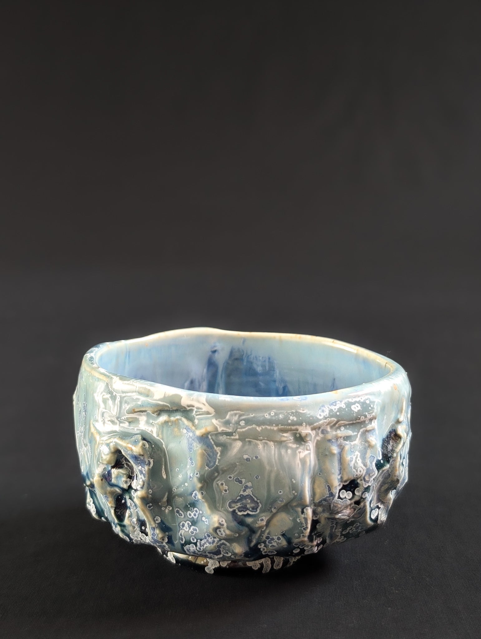 Side view of 'Caldera Bloom', where glaze appears to flow like water over a carved stone surface.