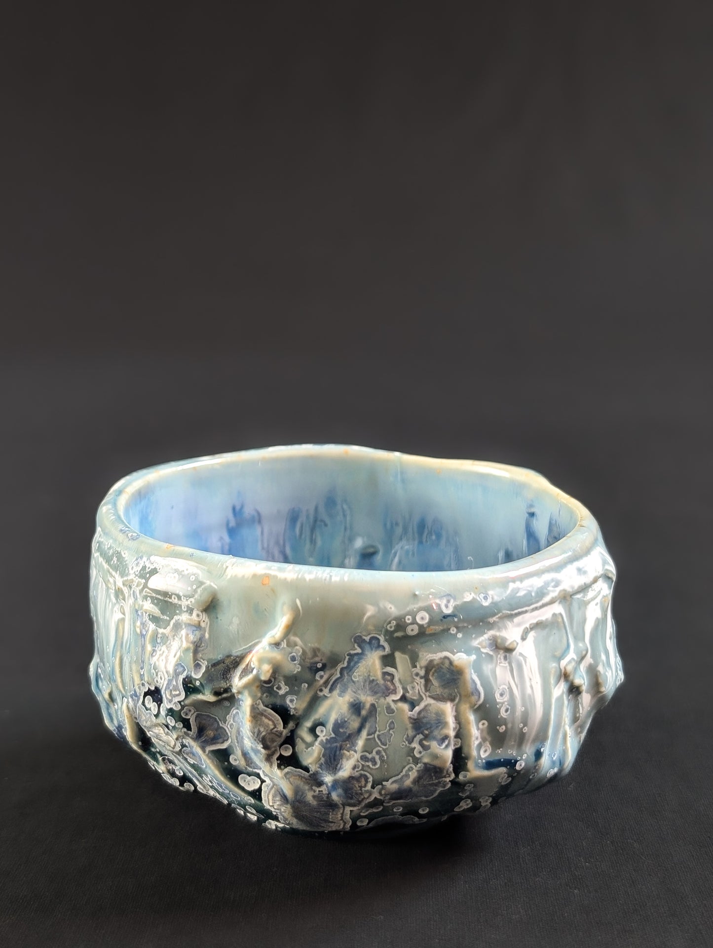 Profile of the chawan with glaze dripping over heavy carving, accented by tiny white-rimmed blue crystals.