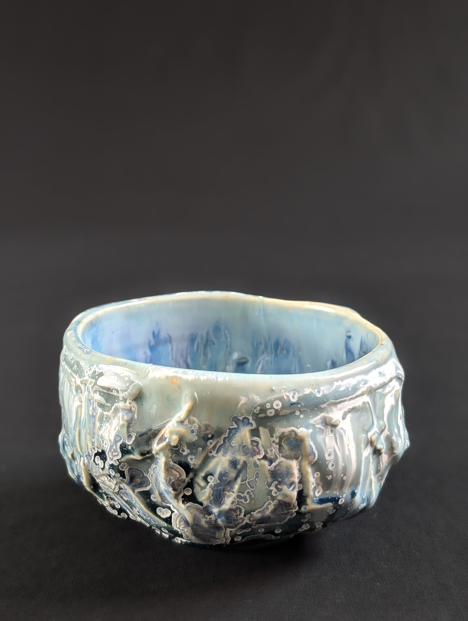 Profile of the chawan with glaze dripping over heavy carving, accented by tiny white-rimmed blue crystals.