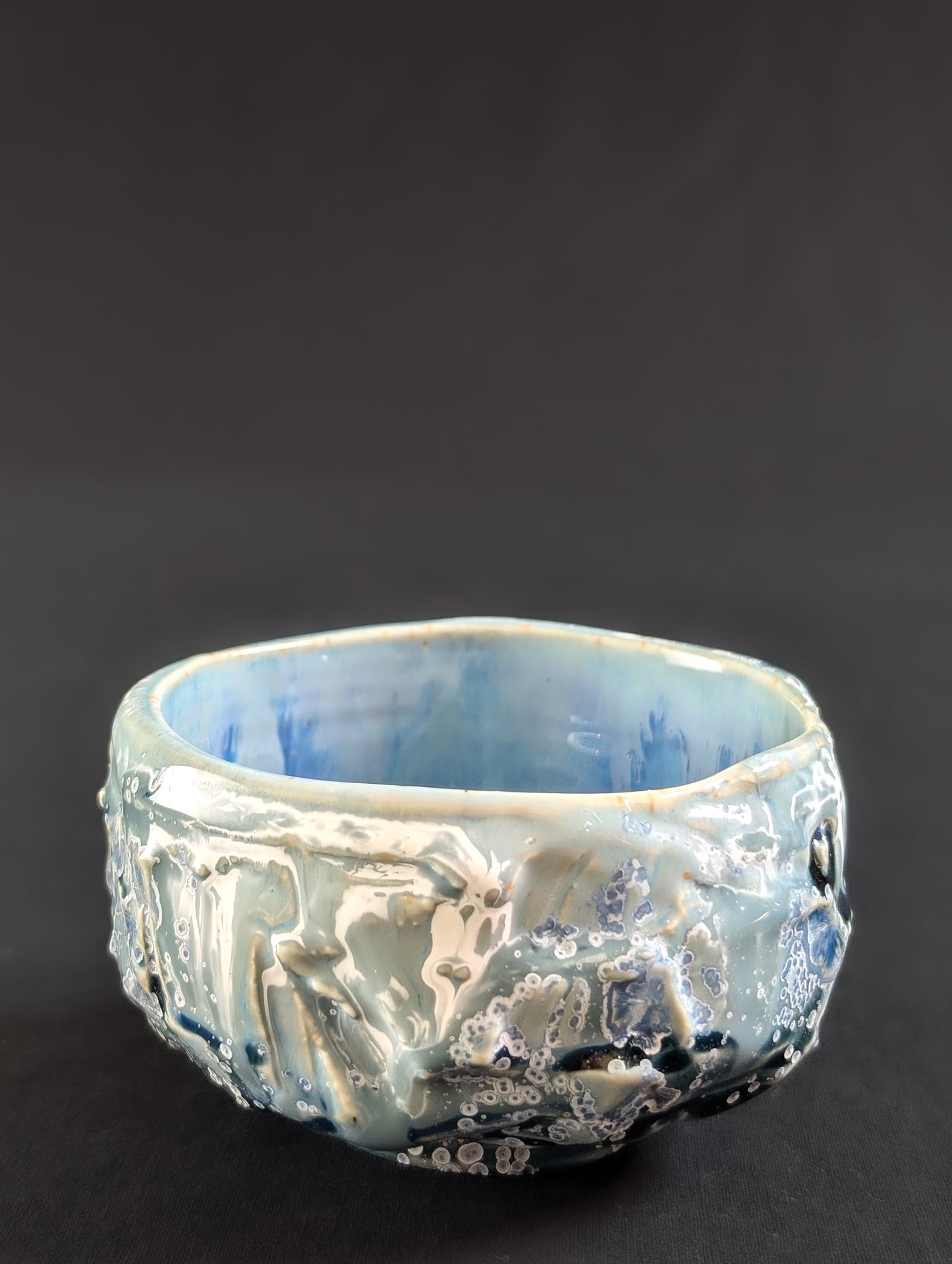 Ceramic tea bowl with textured surface on a dark background.