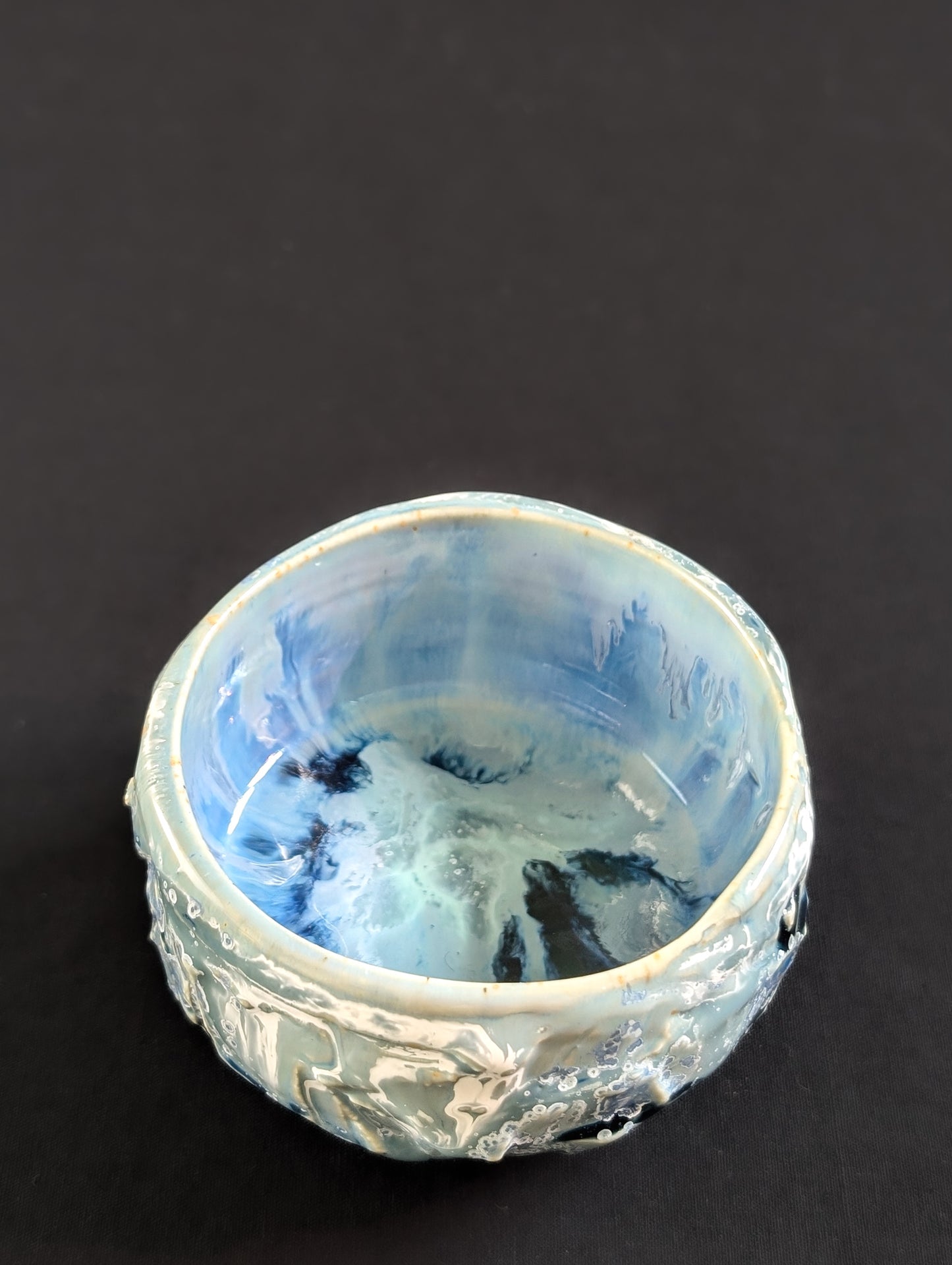Decorative ceramic bowl with blue interior and textured exterior on a black background