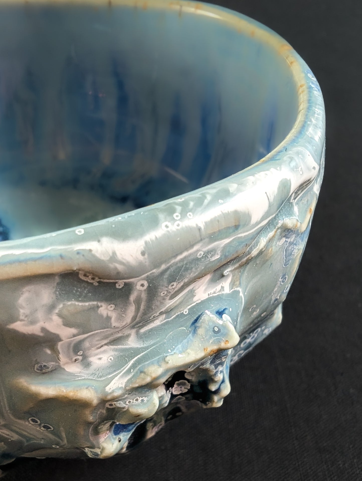 Close-up of the chawan's outer texture, showing small blue crystals and flowing glaze over carved ridges.
