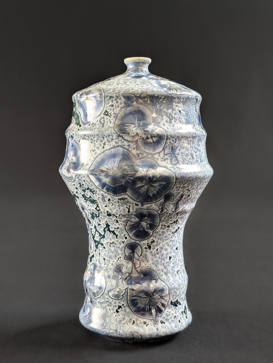 Porcelain vase with blue crystals with silver halo's on a dark background.