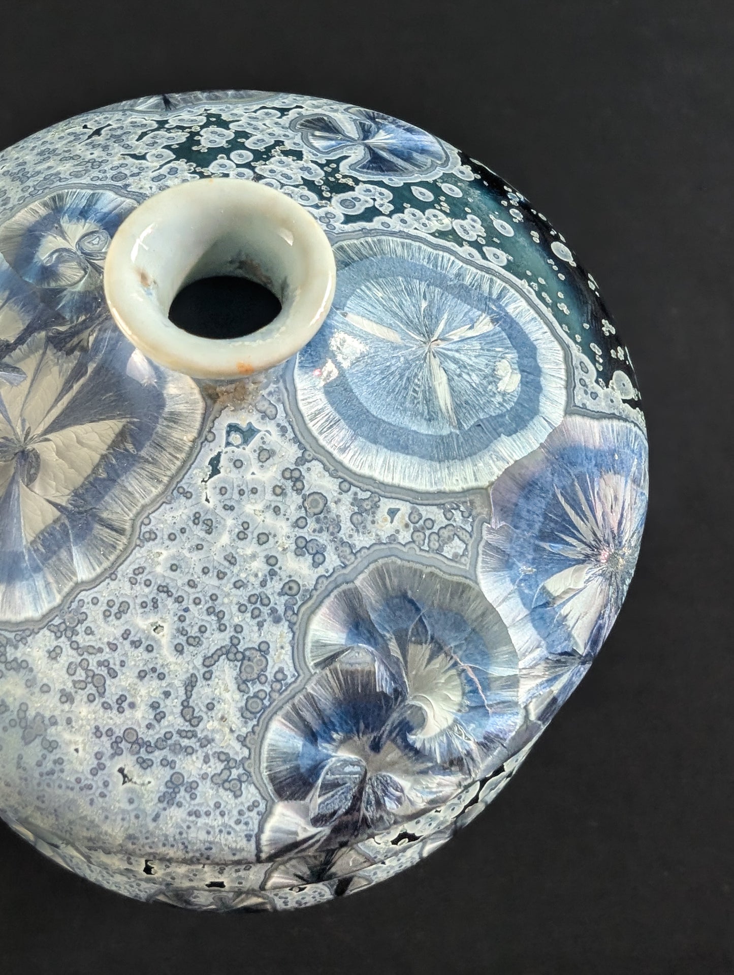 op-down view of a crystalline vase, highlighting the narrow opening and the swirl of blue glaze with silver and lavender crystal patterns radiating across the shoulder.