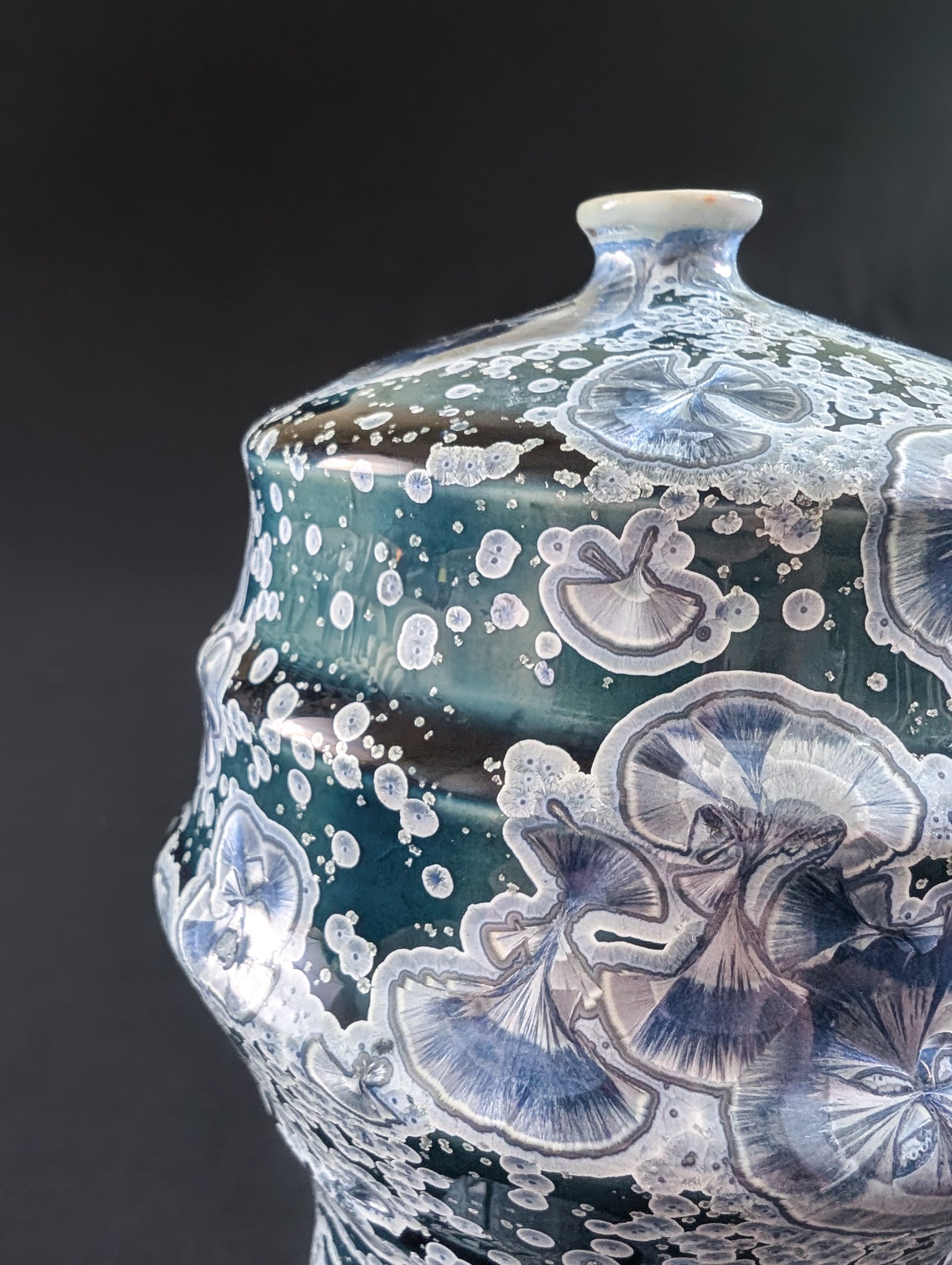 Close-up of the upper section of a crystalline vase, showing detailed silver and lavender crystal blooms floating on a rich midnight blue glaze.