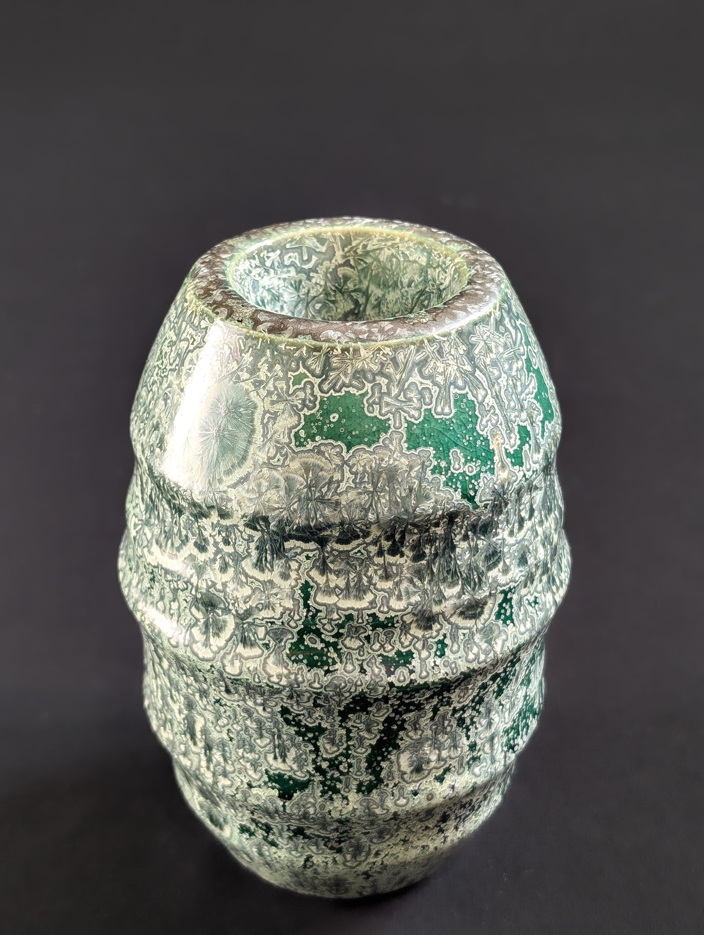 Crystalline glazed vase in emerald green with silver crystal formations, shown from an elevated angle against a dark background.