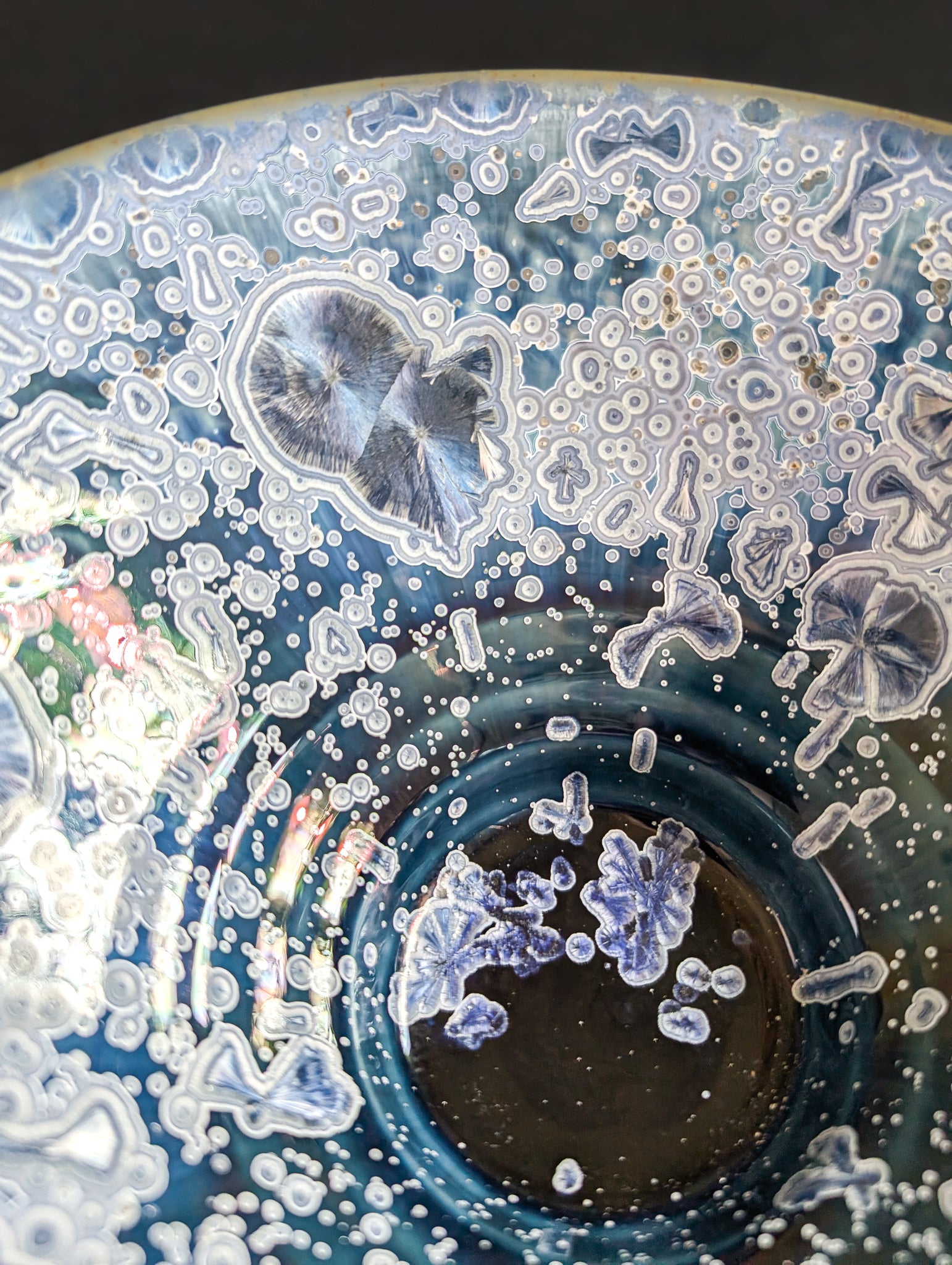 Close up view of sapphire blue crystalline crystals against a deep navy background on the surface of a porcelain ring dish.