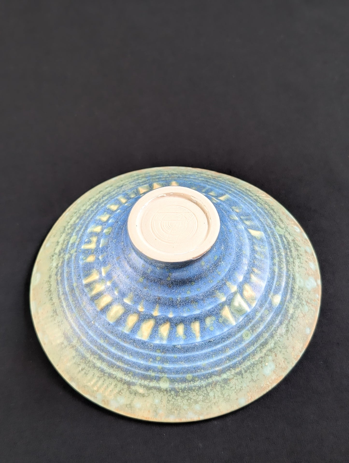 Bottom view of porcelain treasure dish showcasing intricate patterns of green, blue and yellow on a texturized surface.