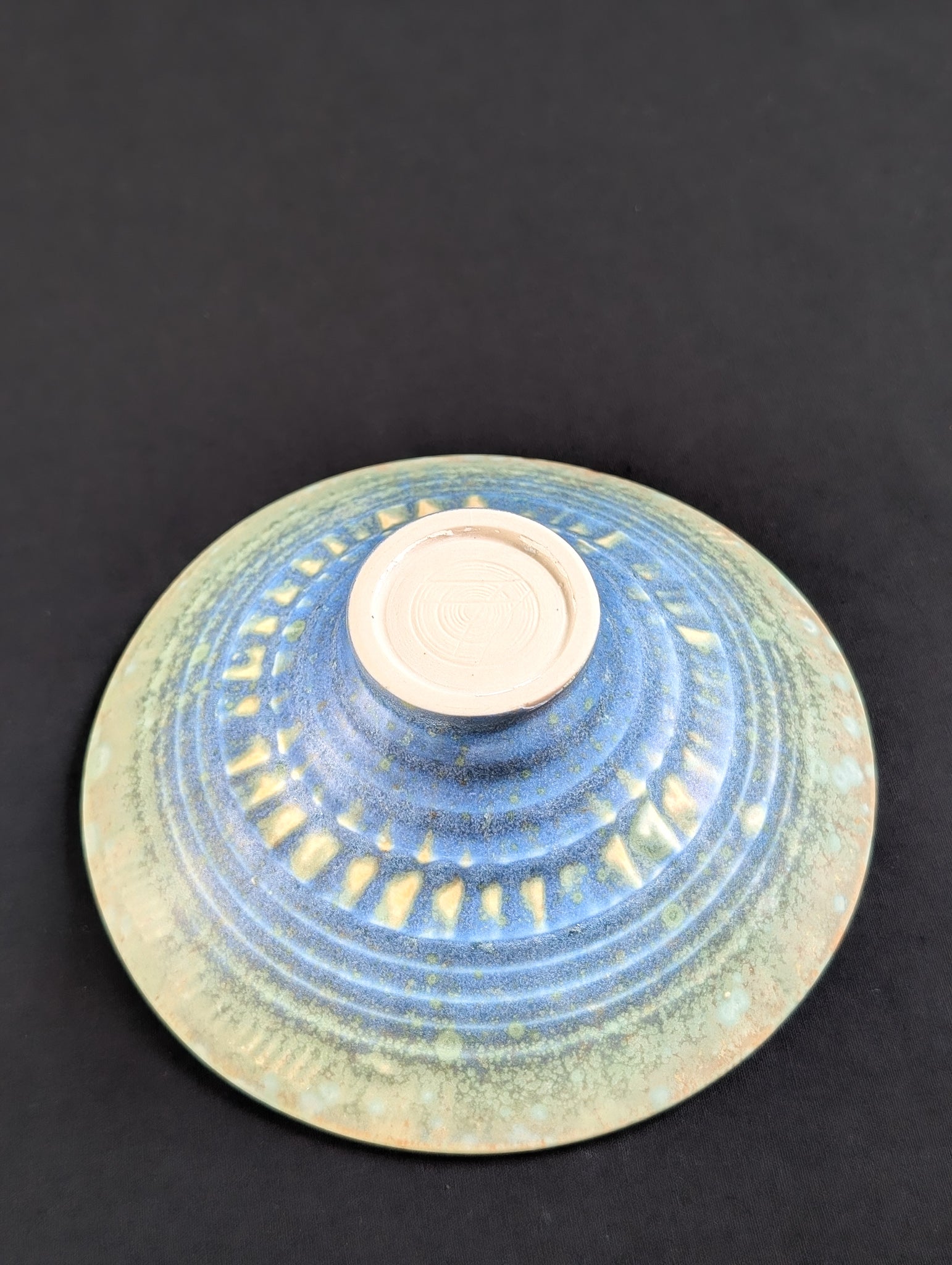 Bottom view of porcelain treasure dish showcasing intricate patterns of green, blue and yellow on a texturized surface.