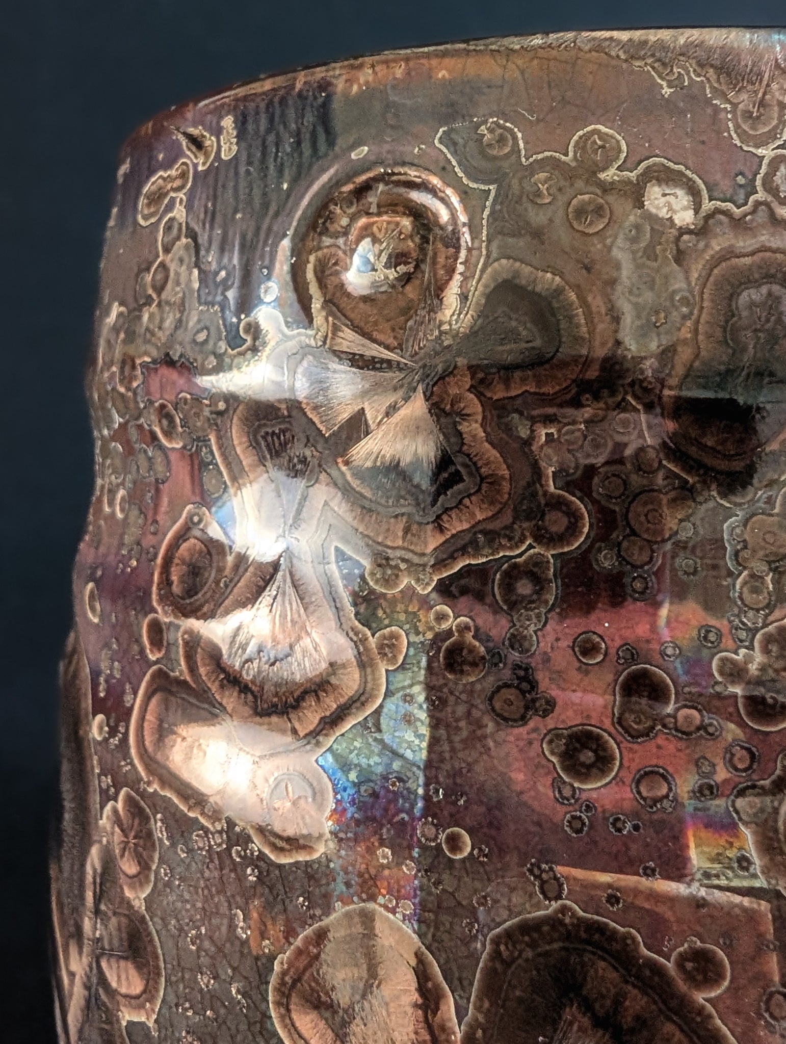 Close-up of a crystalline mug named Ember, highlighting the shimmering rainbow background and the drum key maker’s mark pressed into the glaze near the rim.