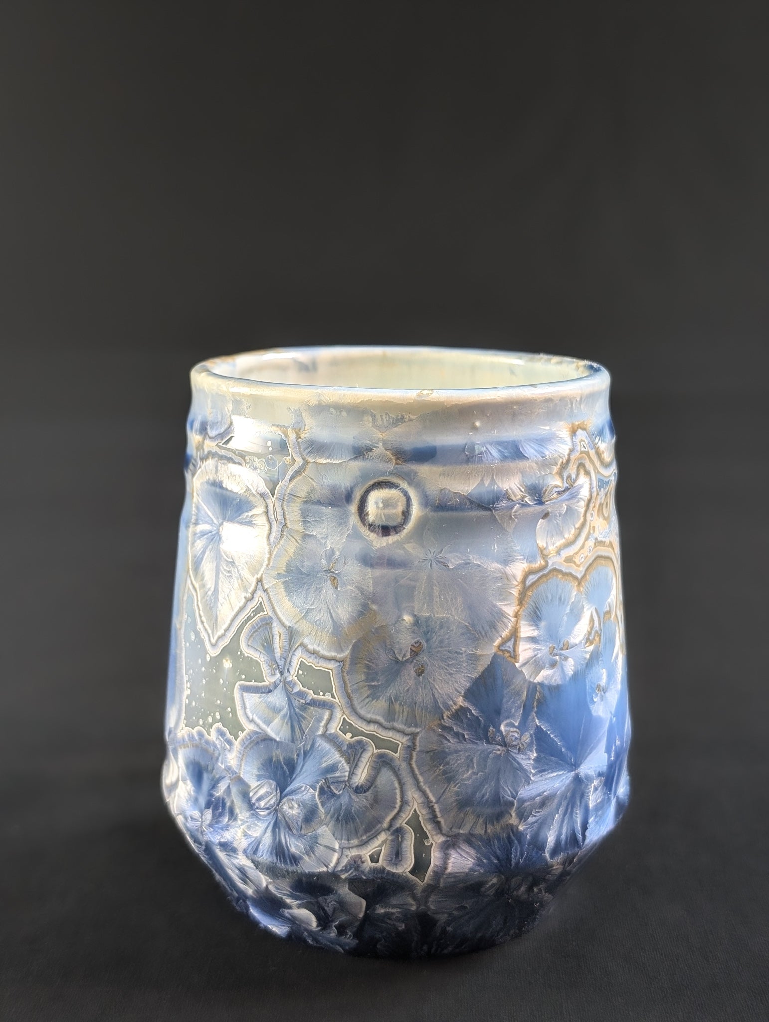 A crystalline glaze mug titled Celestial Atlas, featuring large blue crystal formations over a sky-toned base with gold-ringed details near the rim.