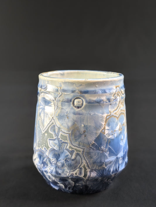 A crystalline glaze mug titled Celestial Atlas, featuring large blue crystal formations over a sky-toned base with gold-ringed details near the rim.