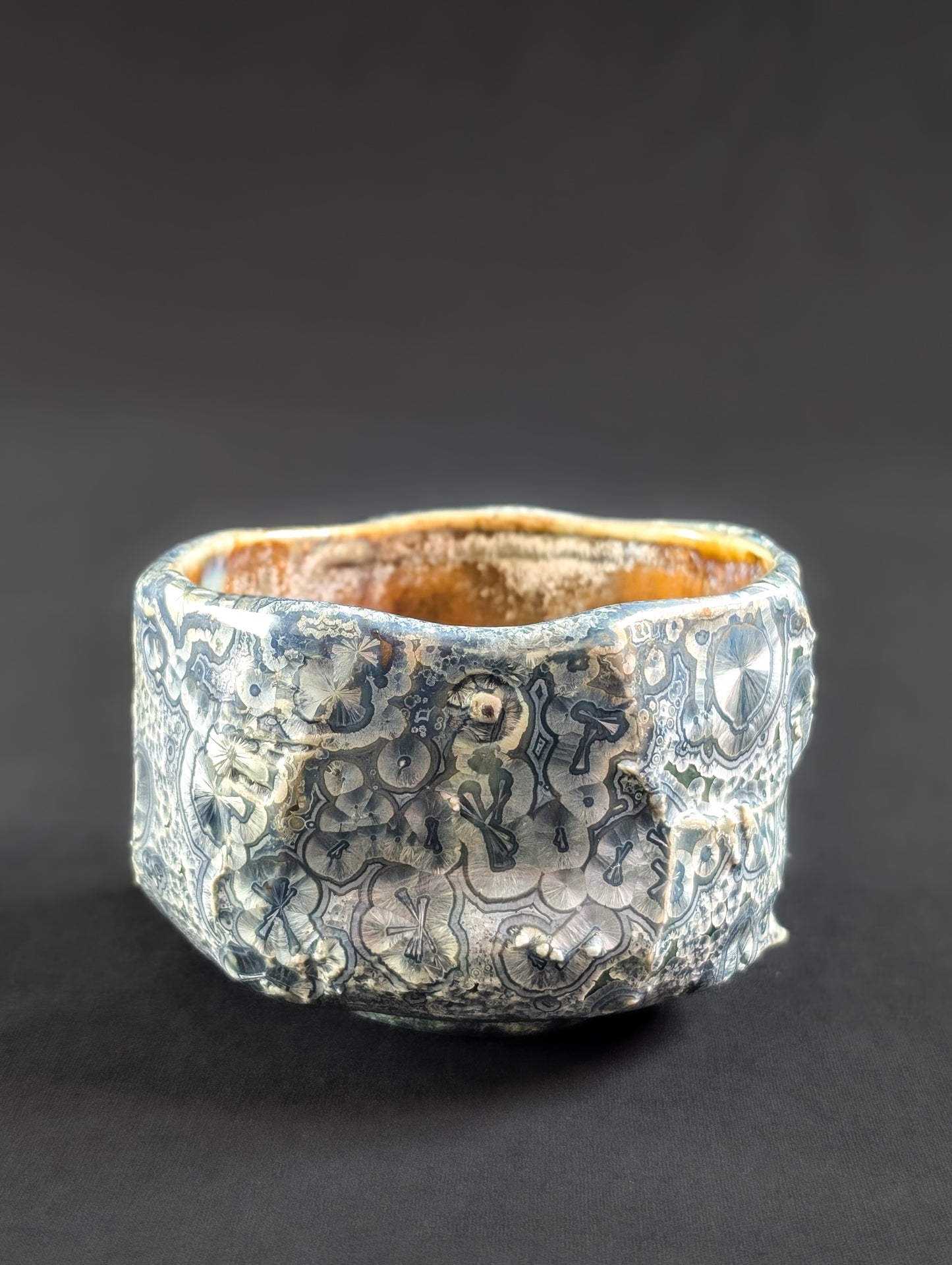 Side view of 'Firevein' chawan by Robbin Harris, showing angular, rock-like carving with blue crystals and white halos over an emerald green glaze.
