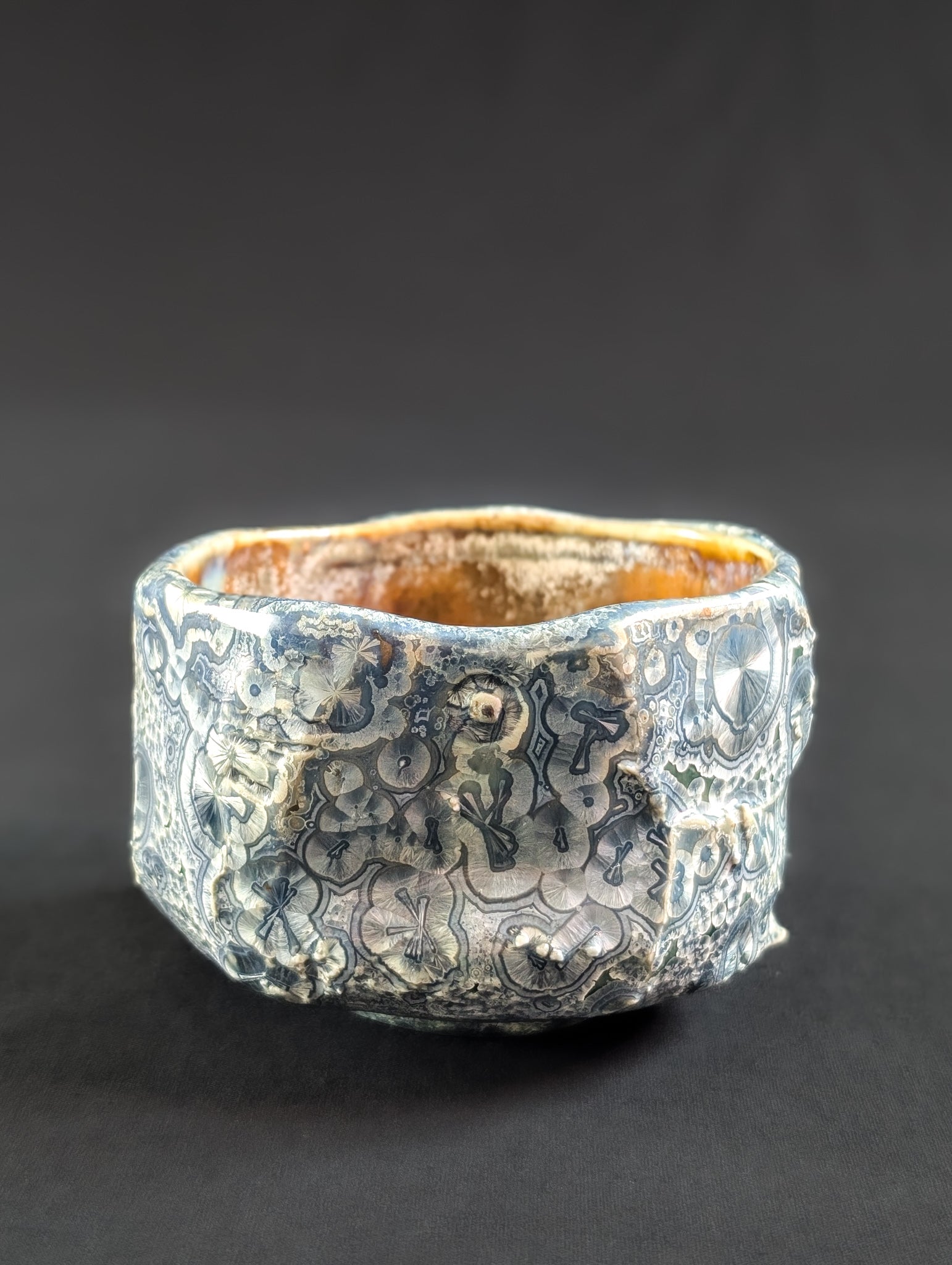 Side view of 'Firevein' chawan by Robbin Harris, showing angular, rock-like carving with blue crystals and white halos over an emerald green glaze.
