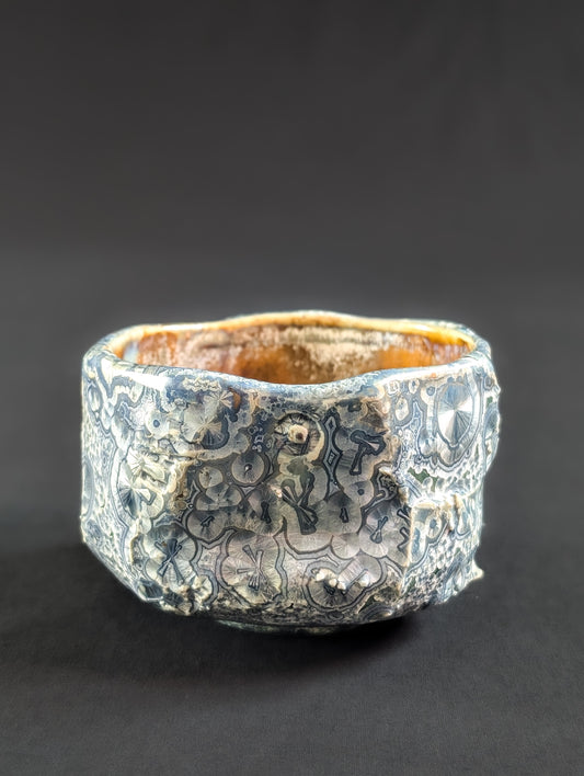 Side view of 'Firevein' chawan by Robbin Harris, showing angular, rock-like carving with blue crystals and white halos over an emerald green glaze.