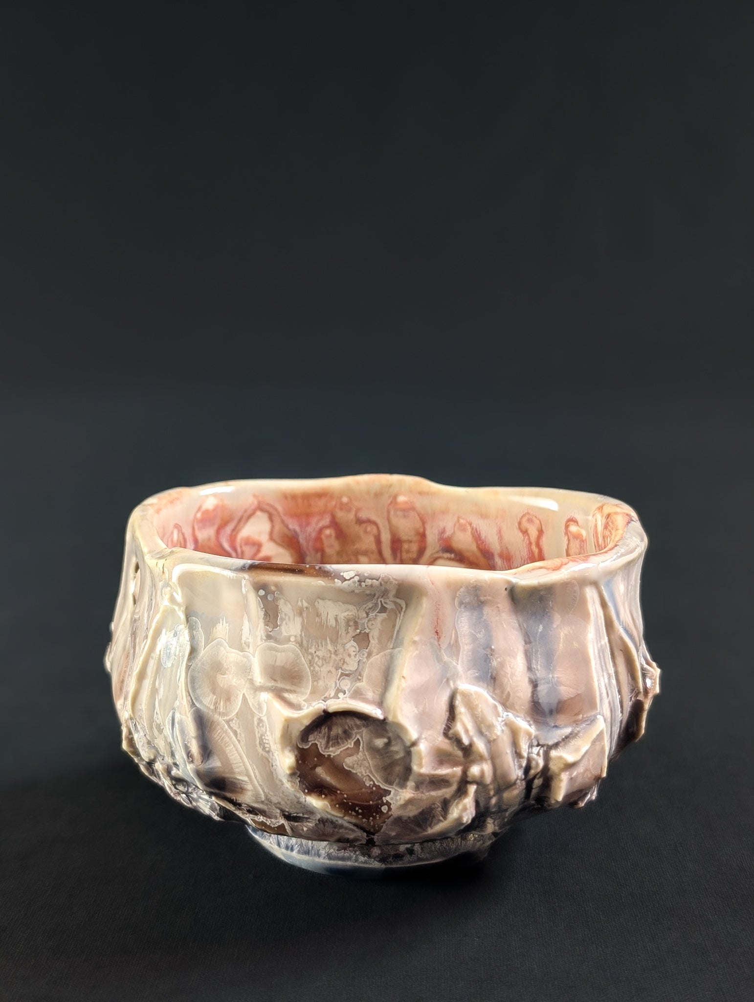 Profile of 'Cliff Rose' tea bowl, with cliff-like carving and delicate light pink glaze flowing over the surface.