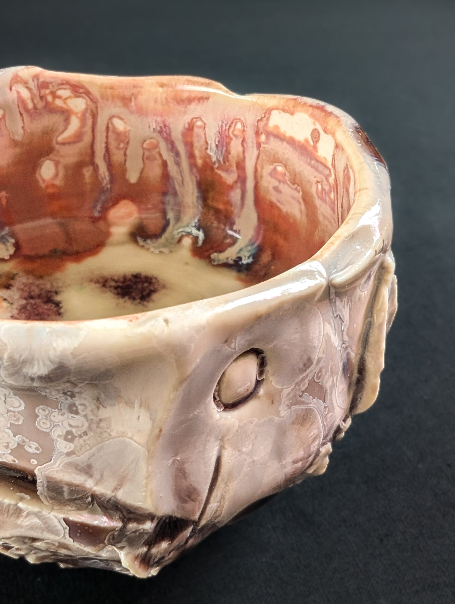 Macro shot of the textured surface where pink glaze pools in crevices and fine crystalline blooms shimmer softly.