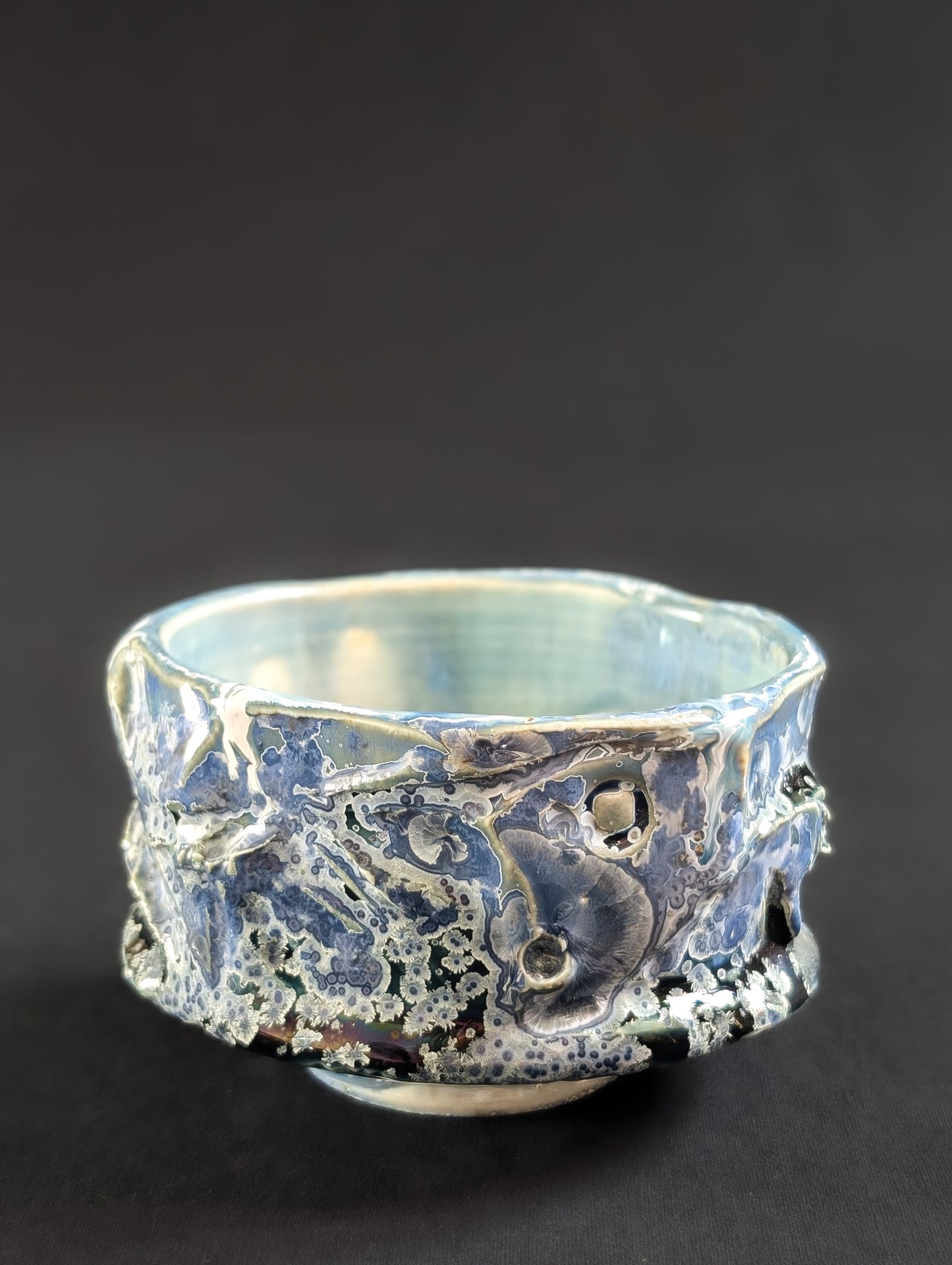 Side view of the 'Nightsky' chawan by Robbin Harris, showing small pale blue crystals with white halos against a deep blue background and heavily textured glaze.