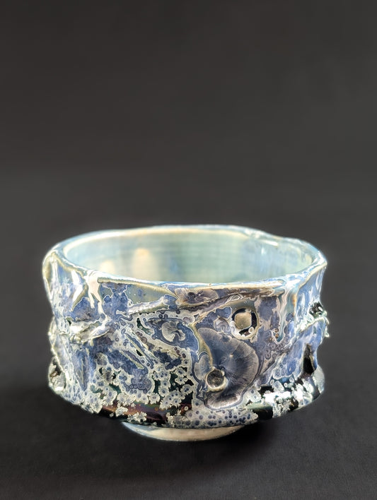 Side view of the 'Nightsky' chawan by Robbin Harris, showing small pale blue crystals with white halos against a deep blue background and heavily textured glaze.
