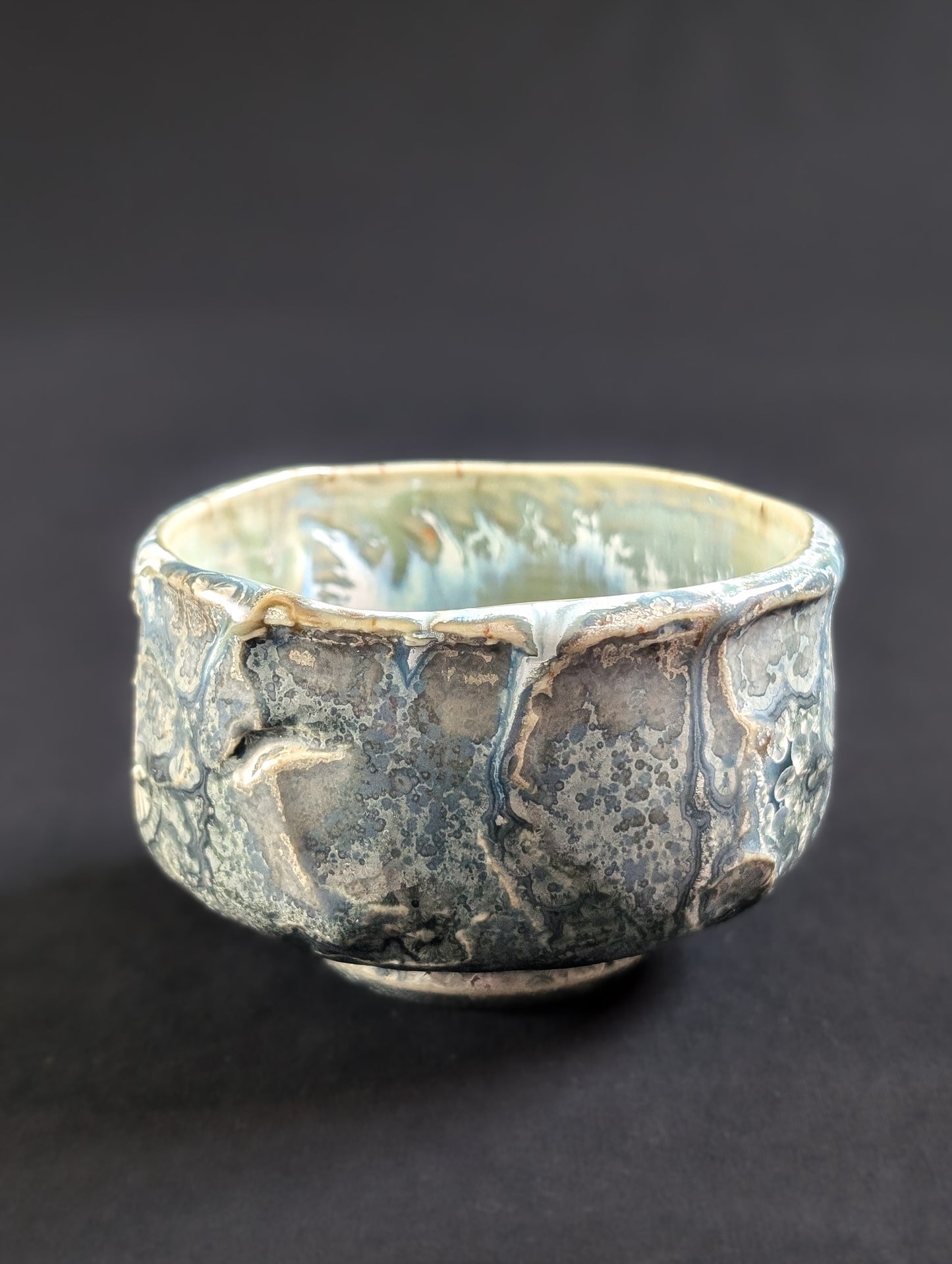 Side view of the 'Tetsuya' chawan by Robbin Harris, featuring a muted gray-blue glaze with small silver-rimmed crystals and cratered, heavily textured surface.