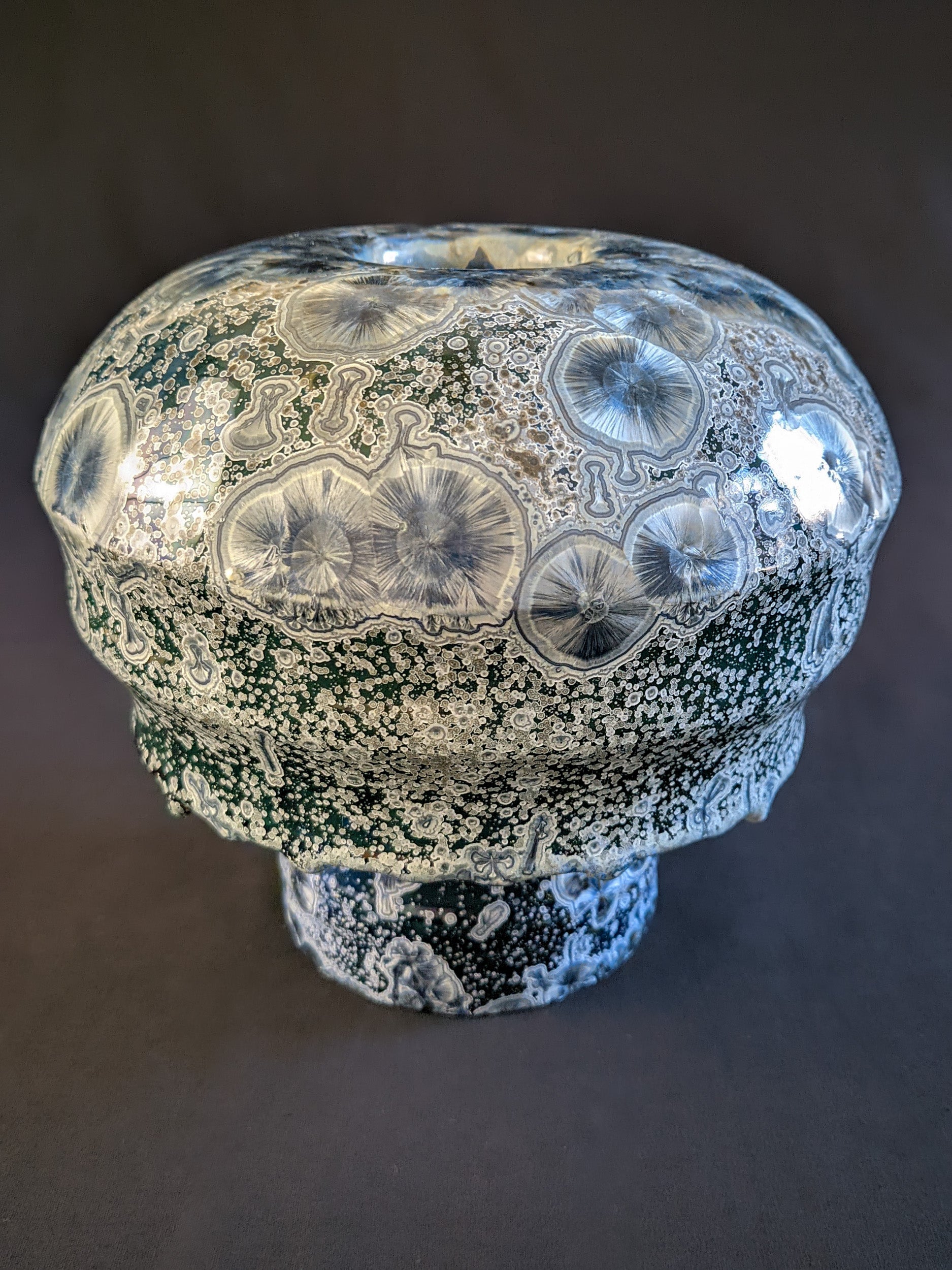 Porcelain vase titled "Milky Green Cosmos," featuring a green gradient background, large deep blue crystals with small silver ones, and a sculptural cap with three parts. The bottom ring is adorned with visible glaze drips.