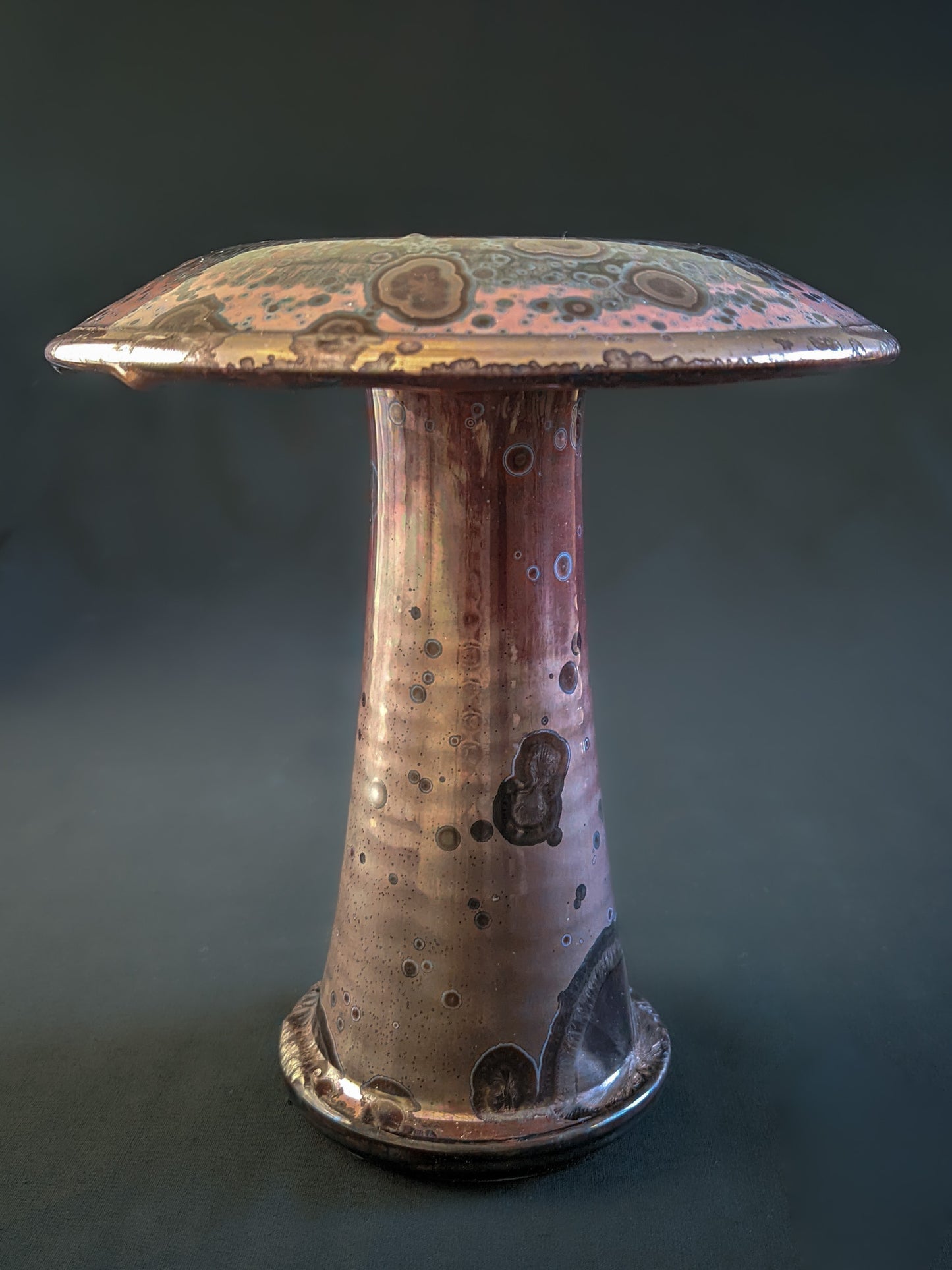 Red ceramic mushroom vase with golden crystals and a shiny rim, created using a reduction firing technique, with a tall, slender shape.