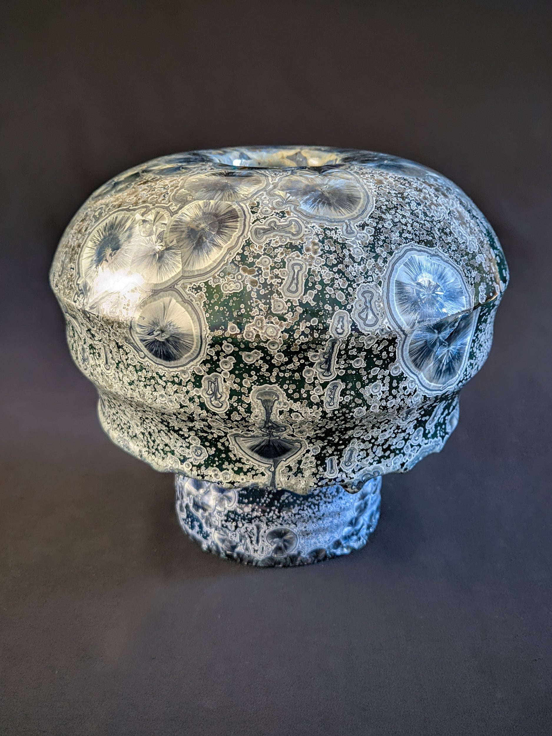 Porcelain vase titled "Milky Green Cosmos," featuring a green gradient background, large deep blue crystals with small silver ones, and a sculptural cap with three parts. The bottom ring is adorned with visible glaze drips.