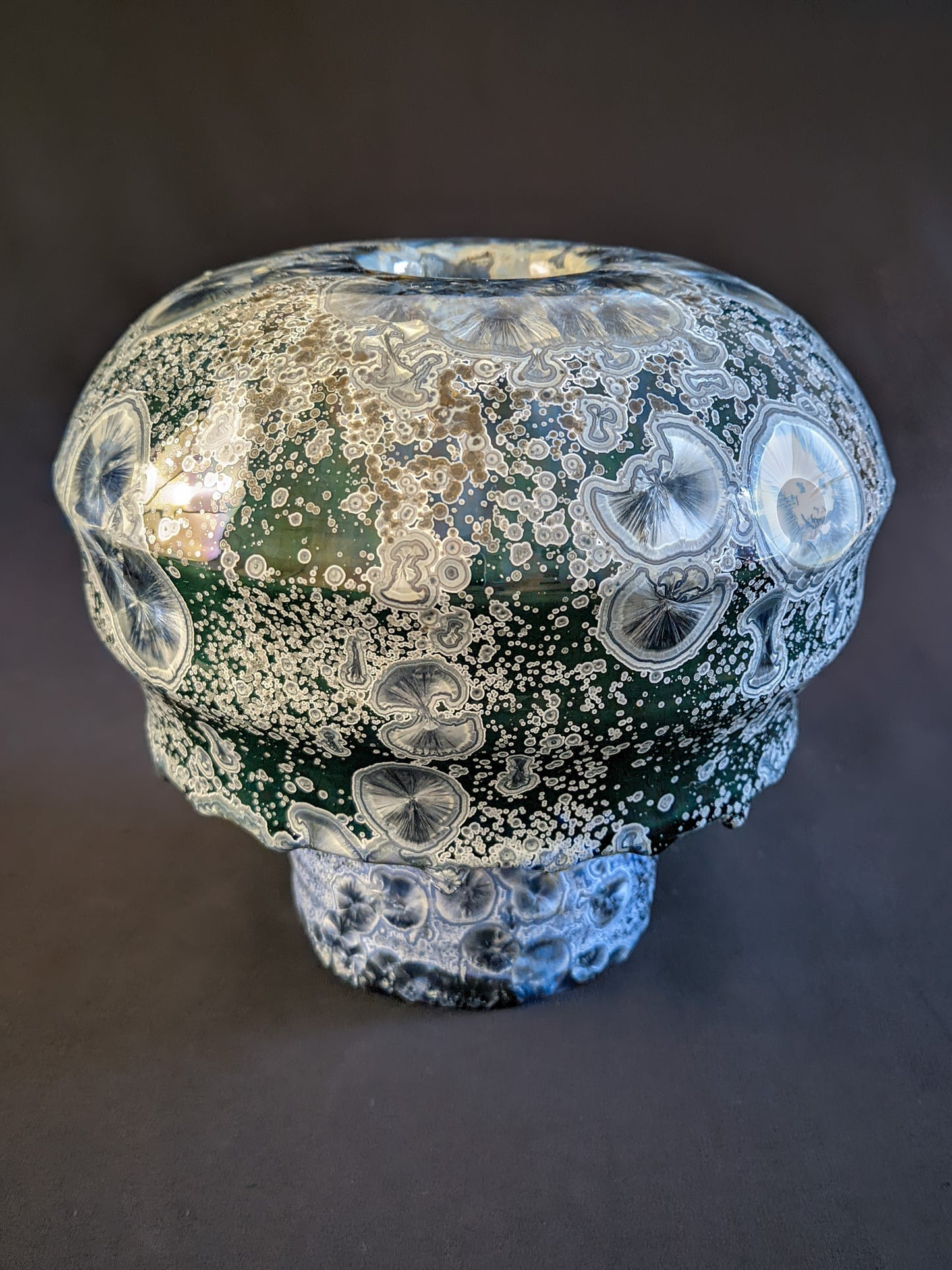 Porcelain vase titled "Milky Green Cosmos," featuring a green gradient background, large deep blue crystals with small silver ones, and a sculptural cap with three parts. The bottom ring is adorned with visible glaze drips.