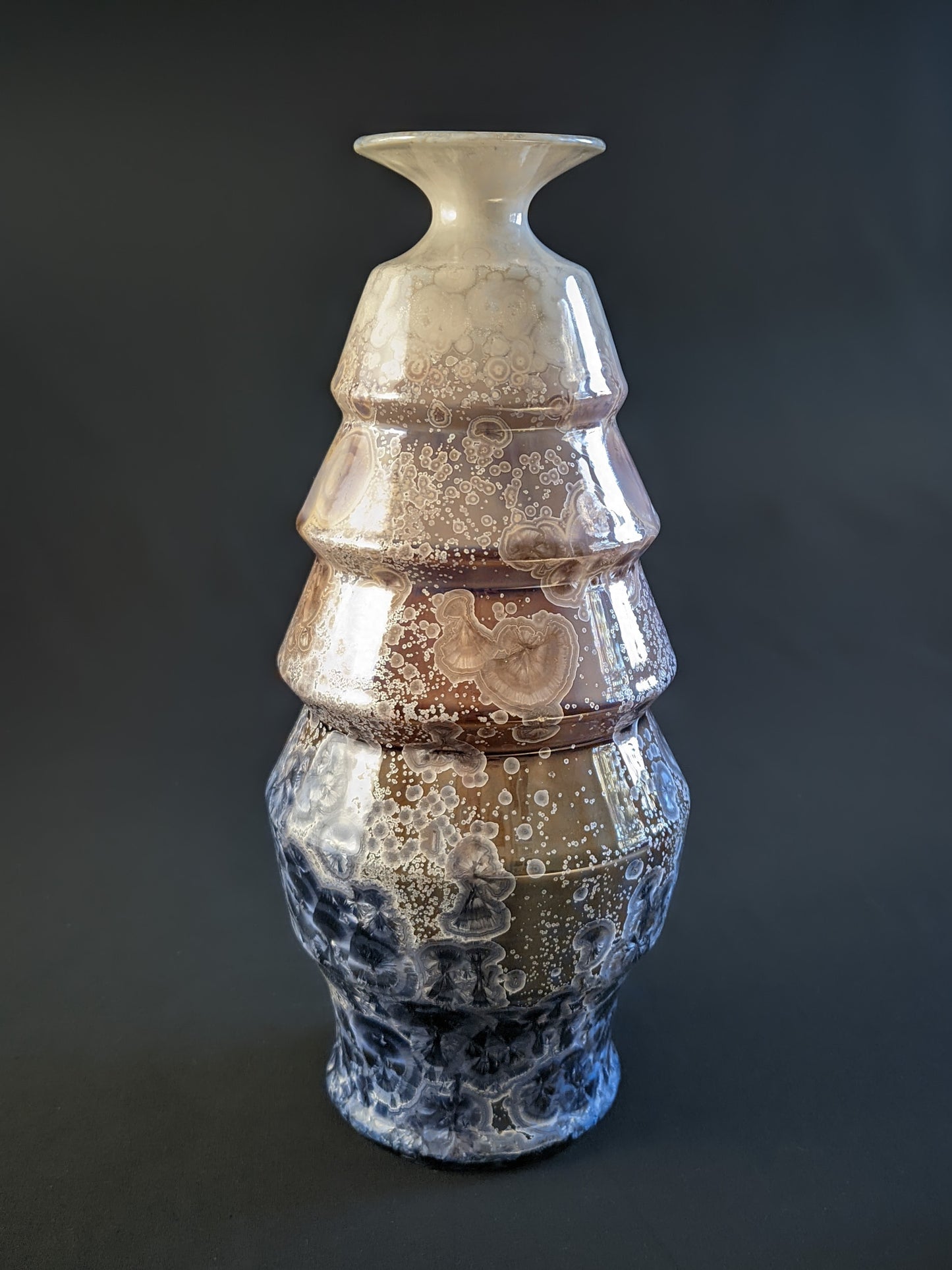 A stunning crystalline-glazed vase named Celestial Cascade, with a tiered, faceted form and intricate starburst-like crystalline patterns in shades of ivory, bronze, blue, and gray.