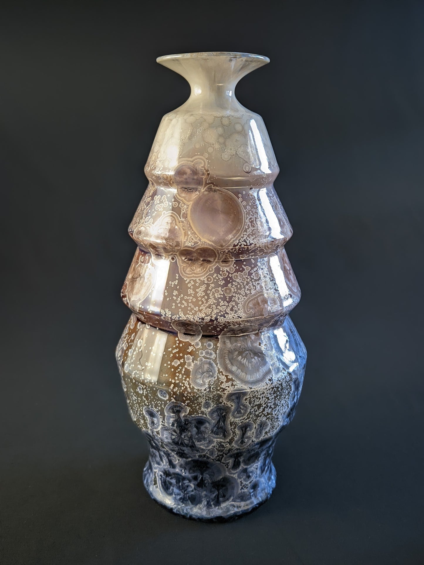 A stunning crystalline-glazed vase named Celestial Cascade, with a tiered, faceted form and intricate starburst-like crystalline patterns in shades of ivory, bronze, blue, and gray.