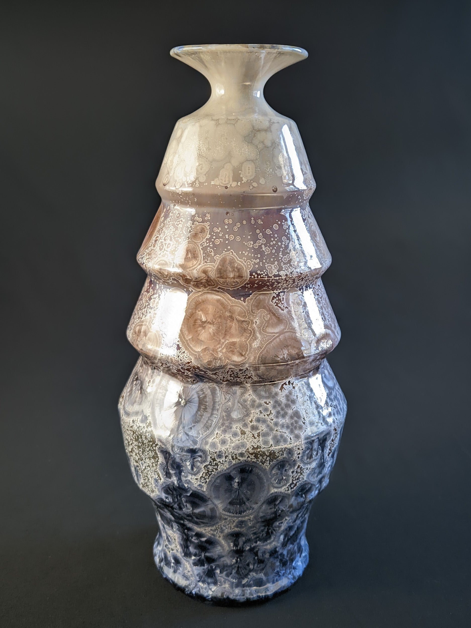 A stunning crystalline-glazed vase named Celestial Cascade, with a tiered, faceted form and intricate starburst-like crystalline patterns in shades of ivory, bronze, blue, and gray.