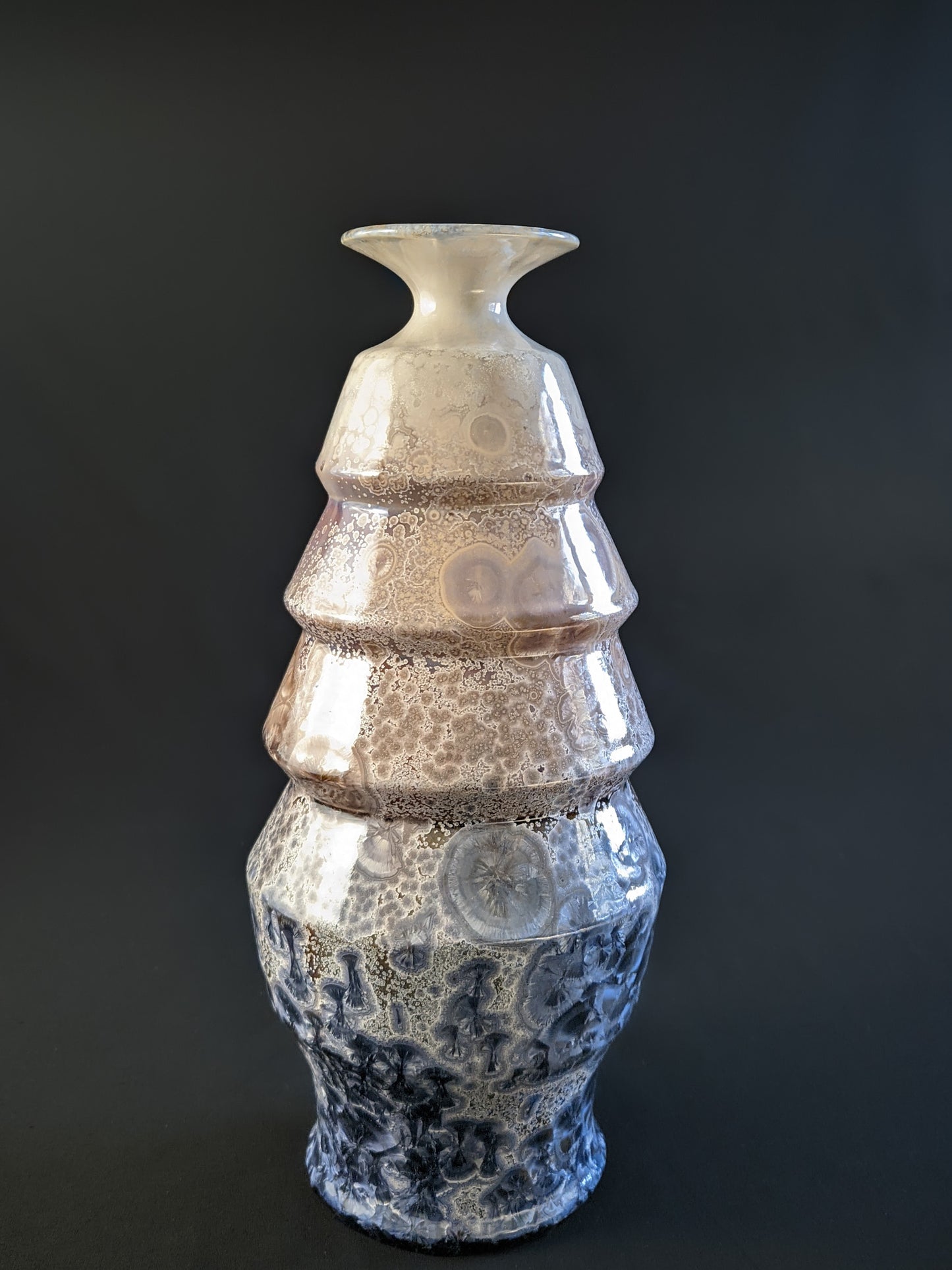 A stunning crystalline-glazed vase named Celestial Cascade, with a tiered, faceted form and intricate starburst-like crystalline patterns in shades of ivory, bronze, blue, and gray.