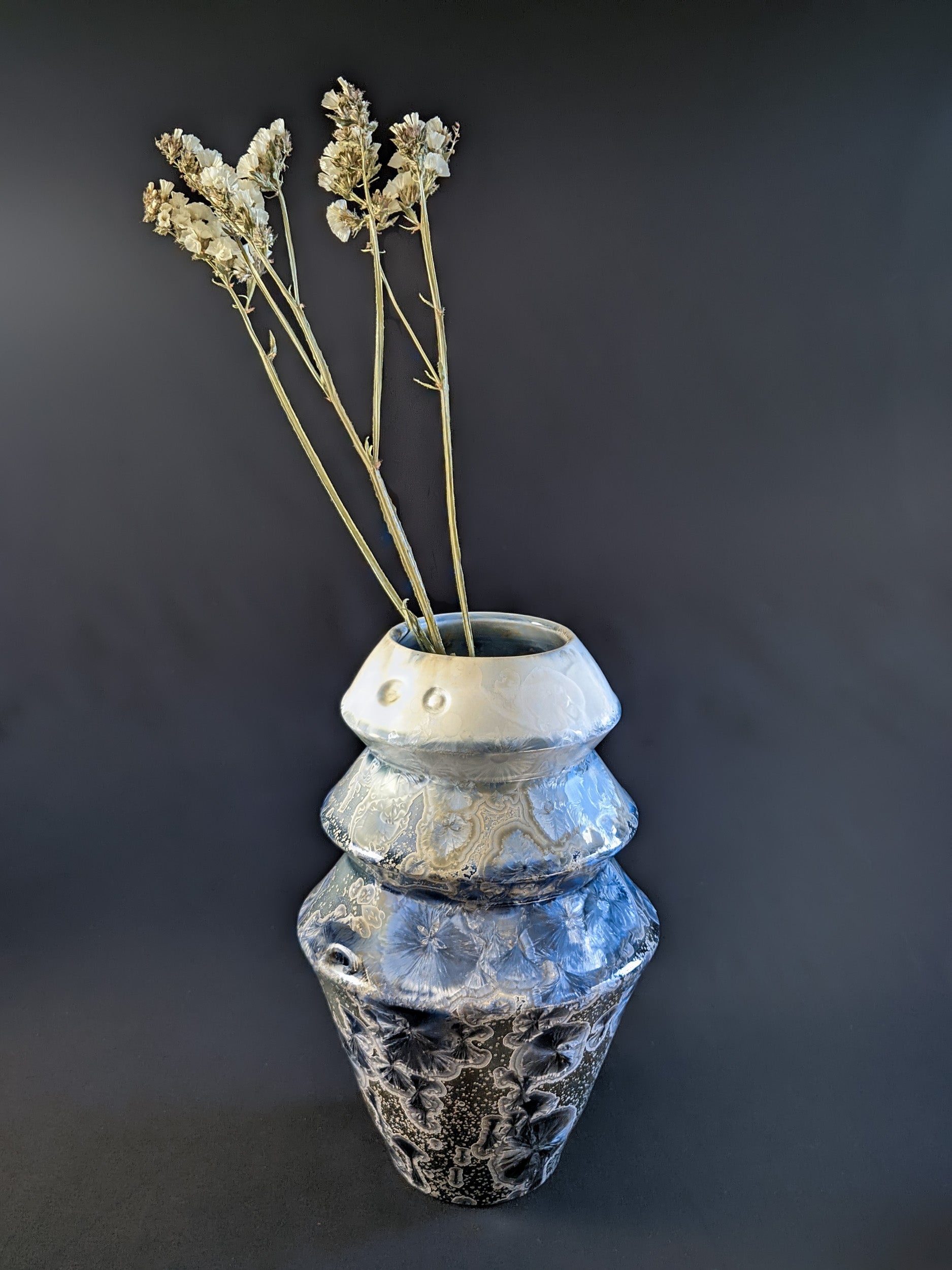 Frozen Serenity vase holding a single dried flower, highlighting the soft gradient from deep blue to pale ivory, with a shimmering crystalline surface.