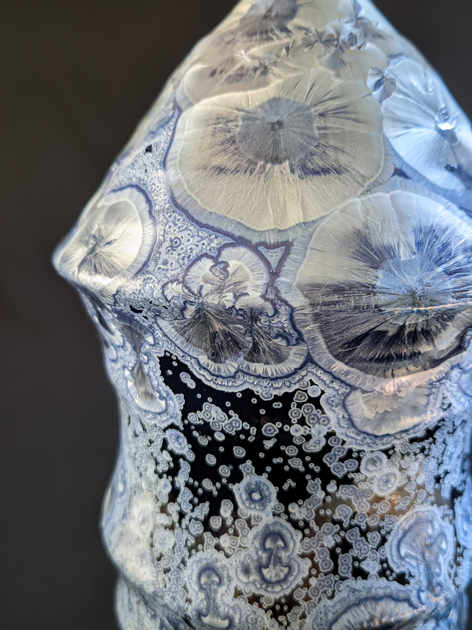 Close up of bottle-shaped ceramic vase with a narrow neck and curved body. Dark blue background with large icy blue crystals and smaller secondary crystals, creating a striking visual effect.