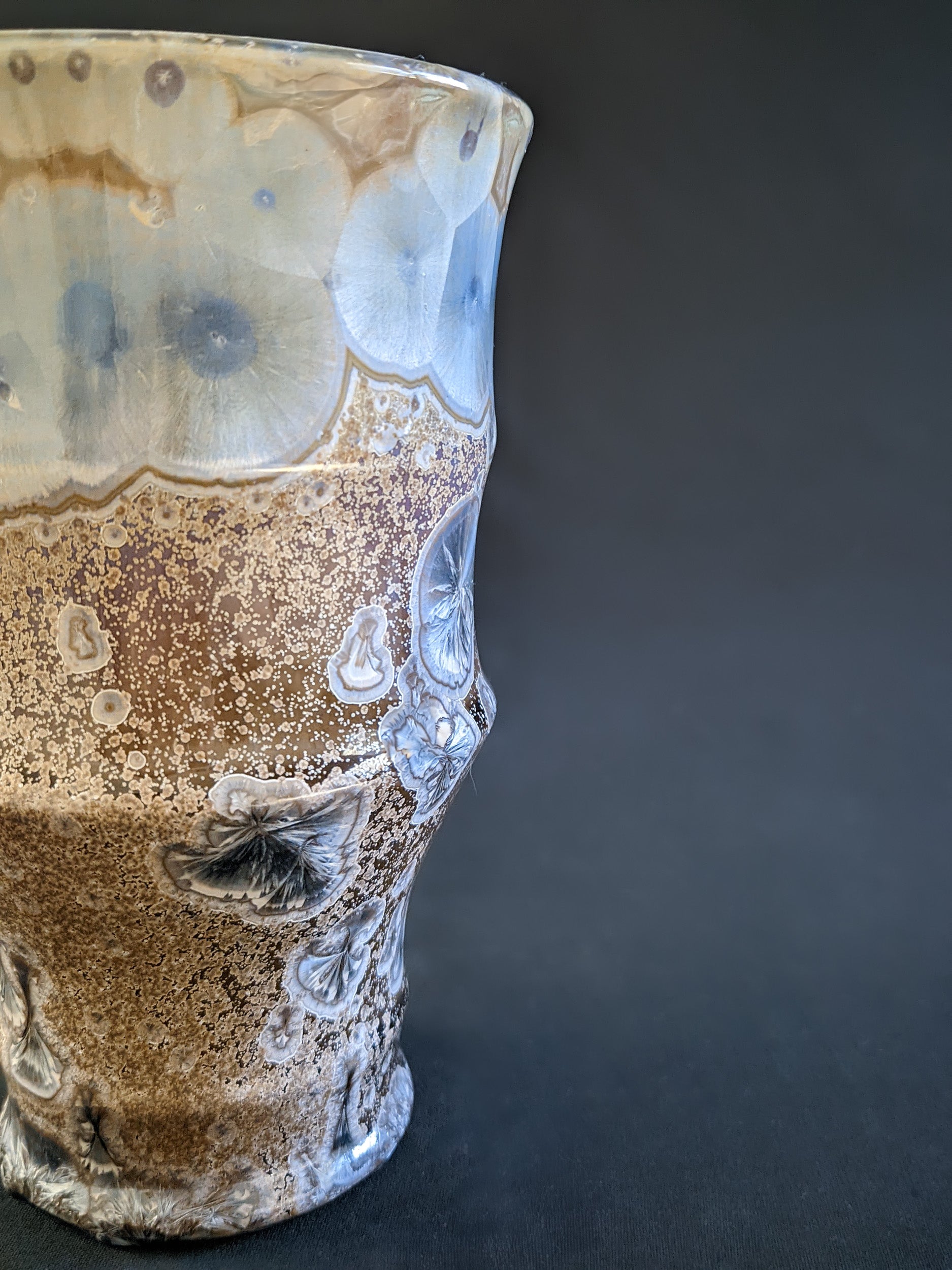 A striking sculptural vessel in amber-brown glaze with metallic blue crystals, displaying a fluid, organic shape with elegant, sweeping curves.